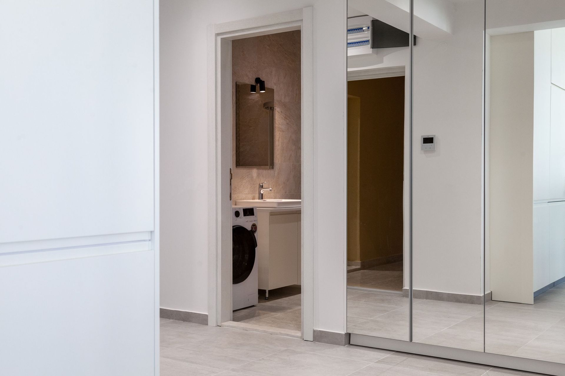 Modern bathroom with a washing machine in an apartment, Kotor, Montenegro: light finishes and a mirrored cabinet.