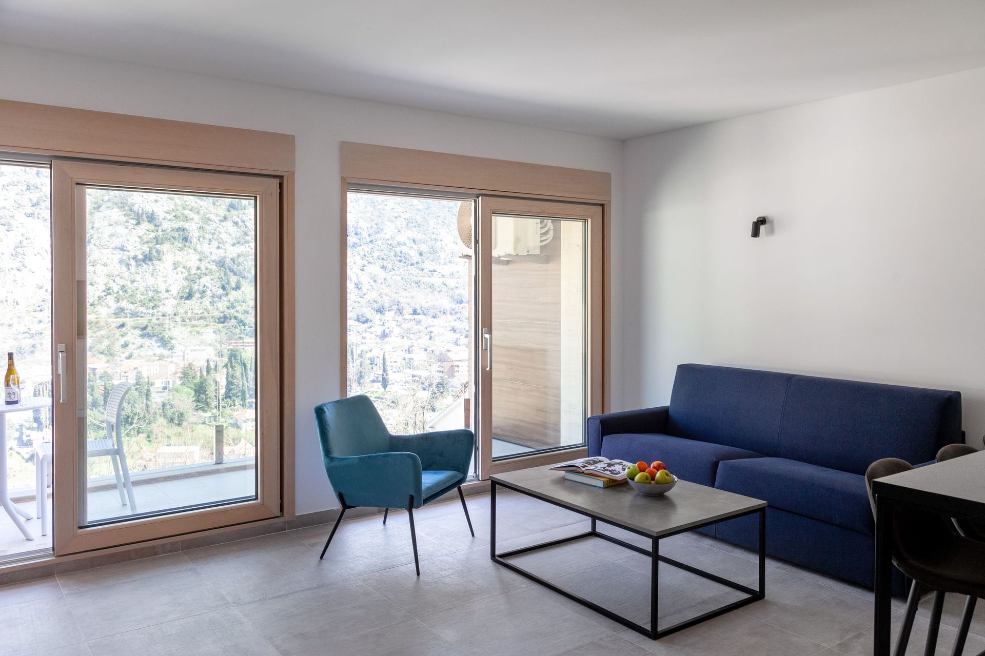 Modern living room in an apartment in Kotor, Montenegro: blue sofa, armchair, panoramic windows with mountain views.