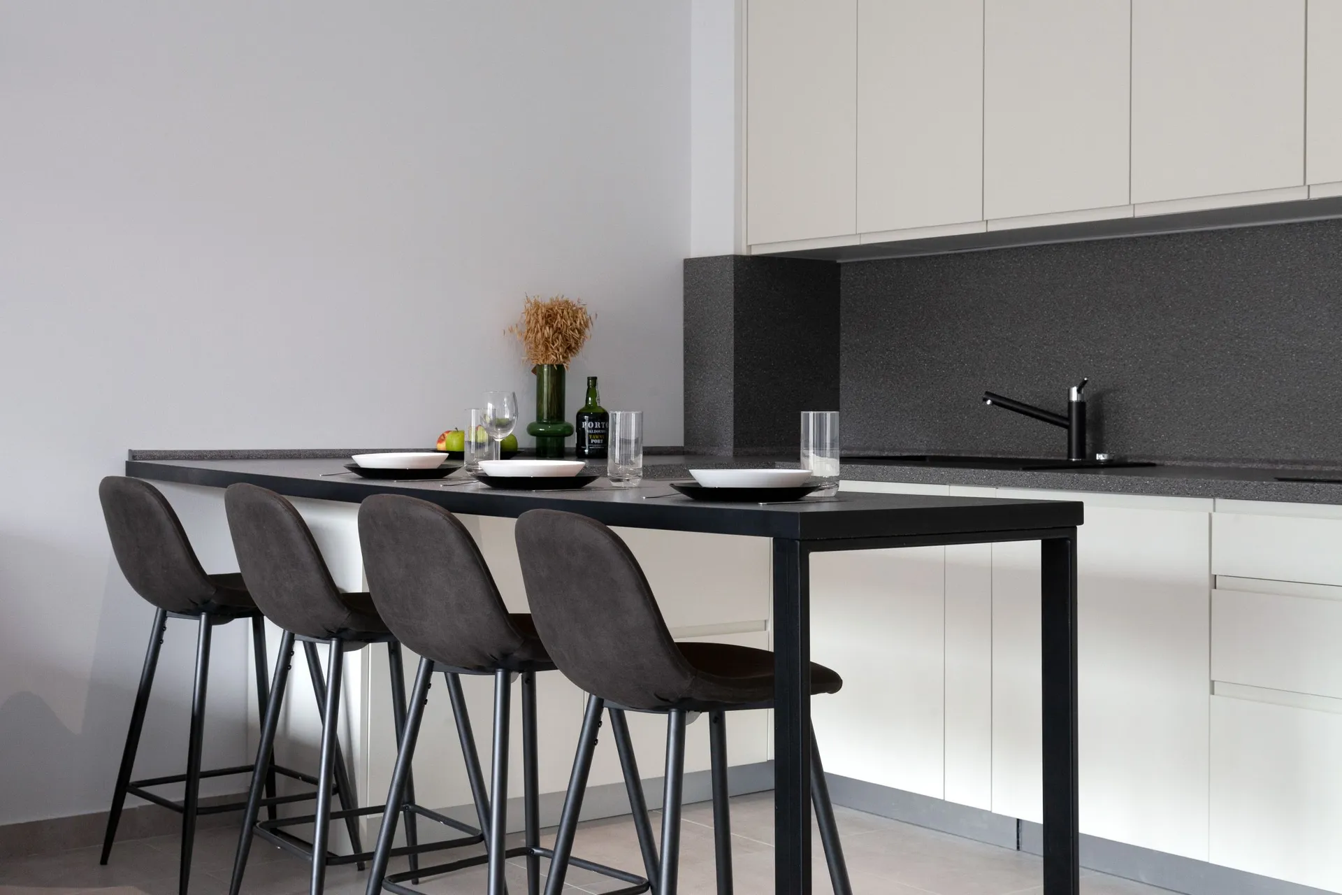 Modern kitchen with a black countertop, white cabinets, and four dark bar stools set for dining.