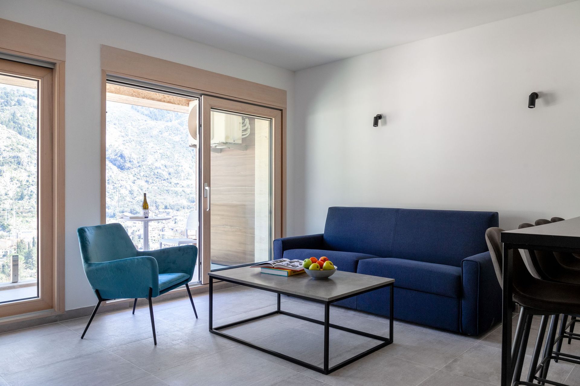 Living room in an apartment in Kotor, Montenegro: blue sofa, armchair, panoramic windows with mountain views, and a terrace.