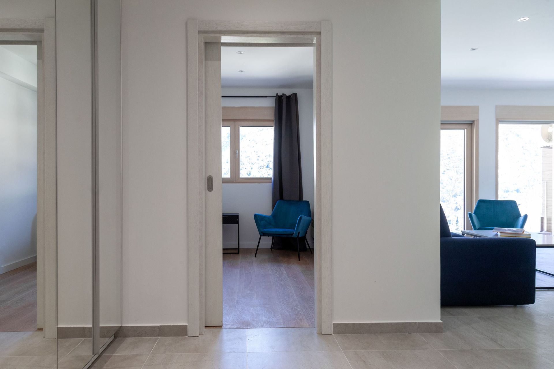 Interior of a modern apartment in Kotor, Montenegro: a bright living room with blue armchairs, wooden flooring, and a view.