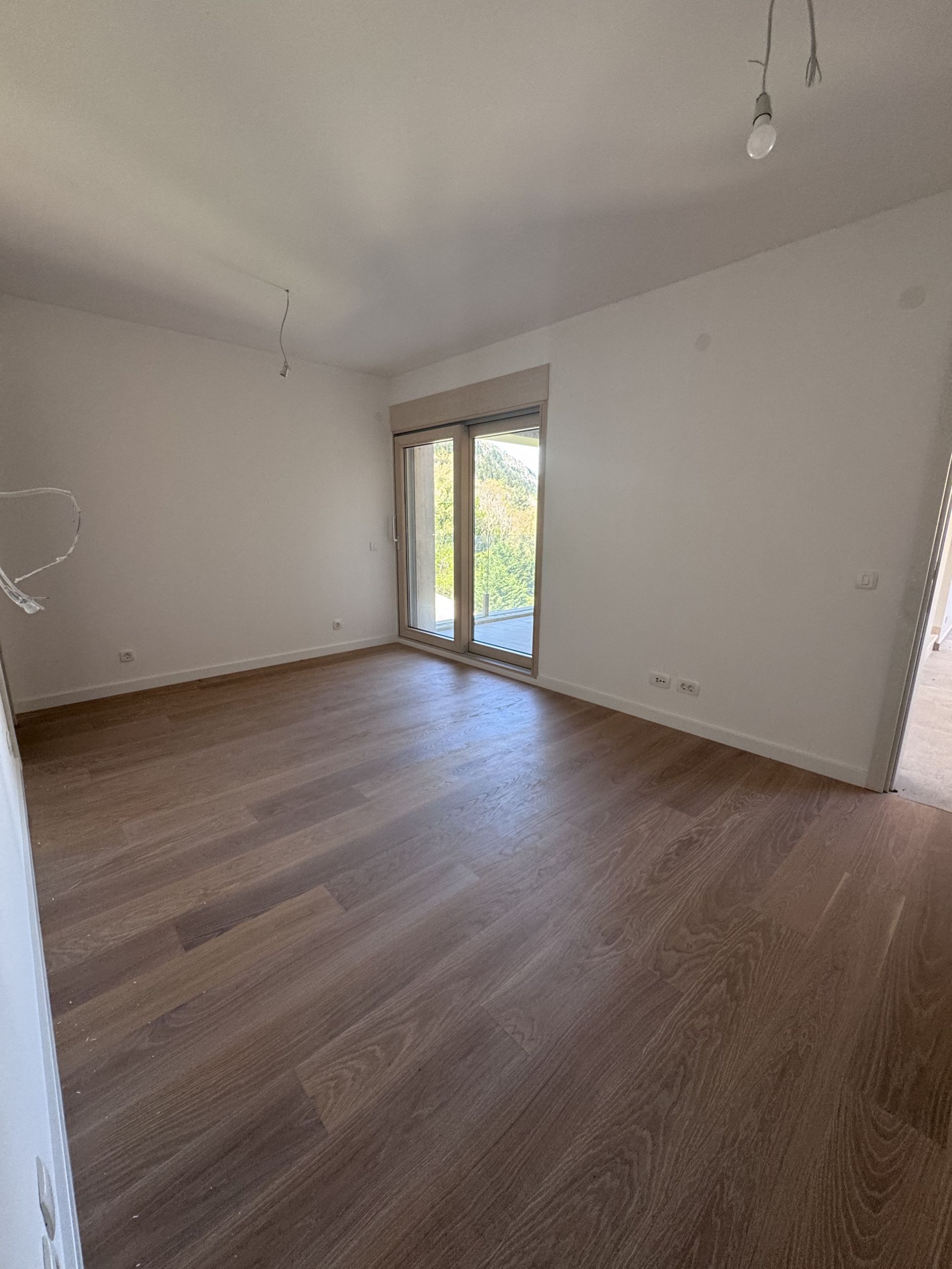 Bright living room in a new apartment in Kotor, Montenegro: parquet floor, white walls, and access to a terrace with a view.
