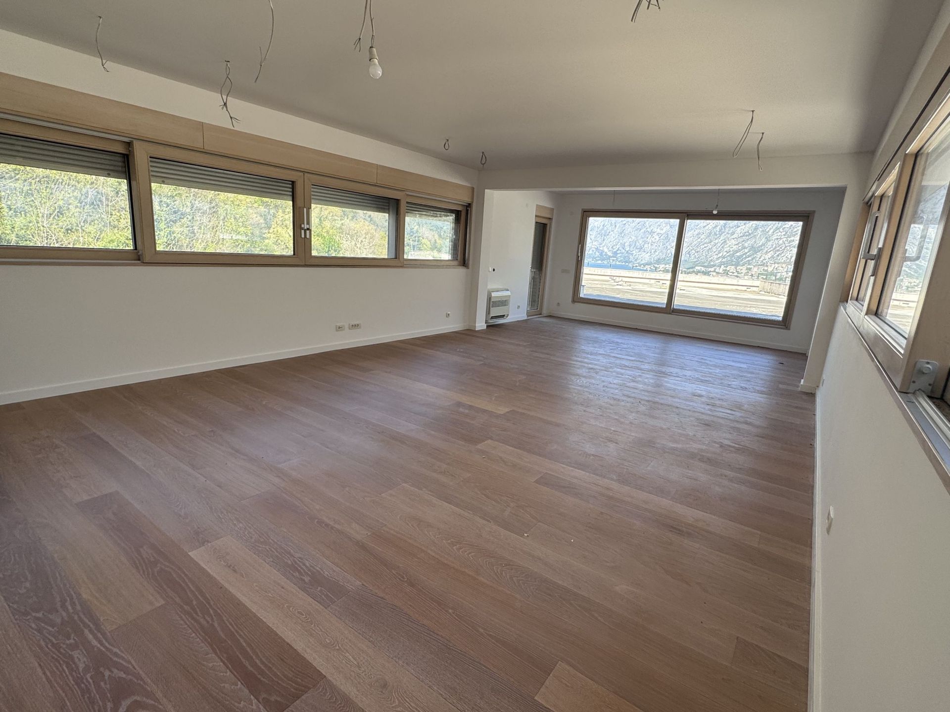 Spacious living room in a duplex, Kotor, Montenegro: panoramic windows, wooden floor, mountain and sea view.