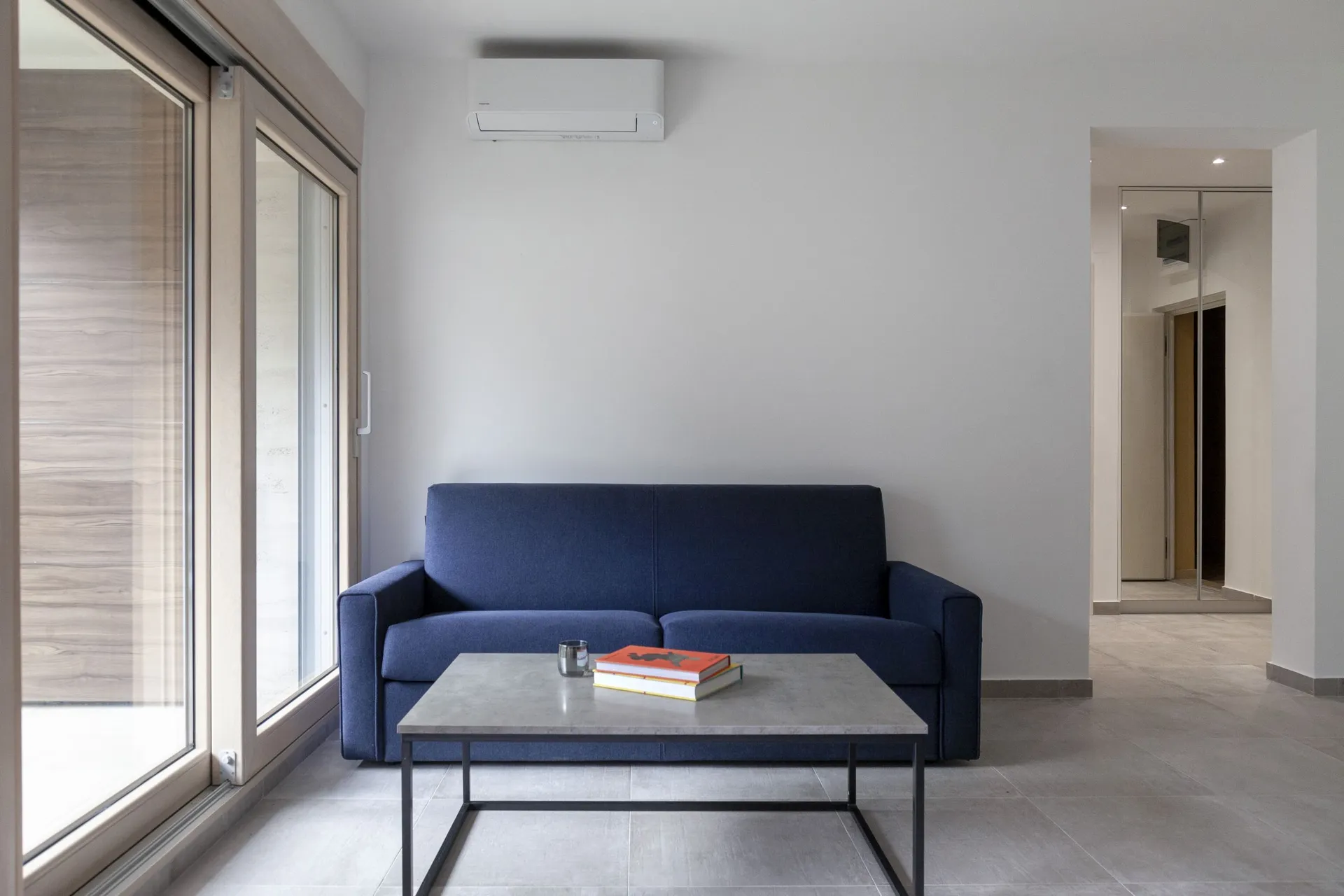 Modern living room with a blue sofa, grey coffee table, and white wall-mounted air conditioner.
