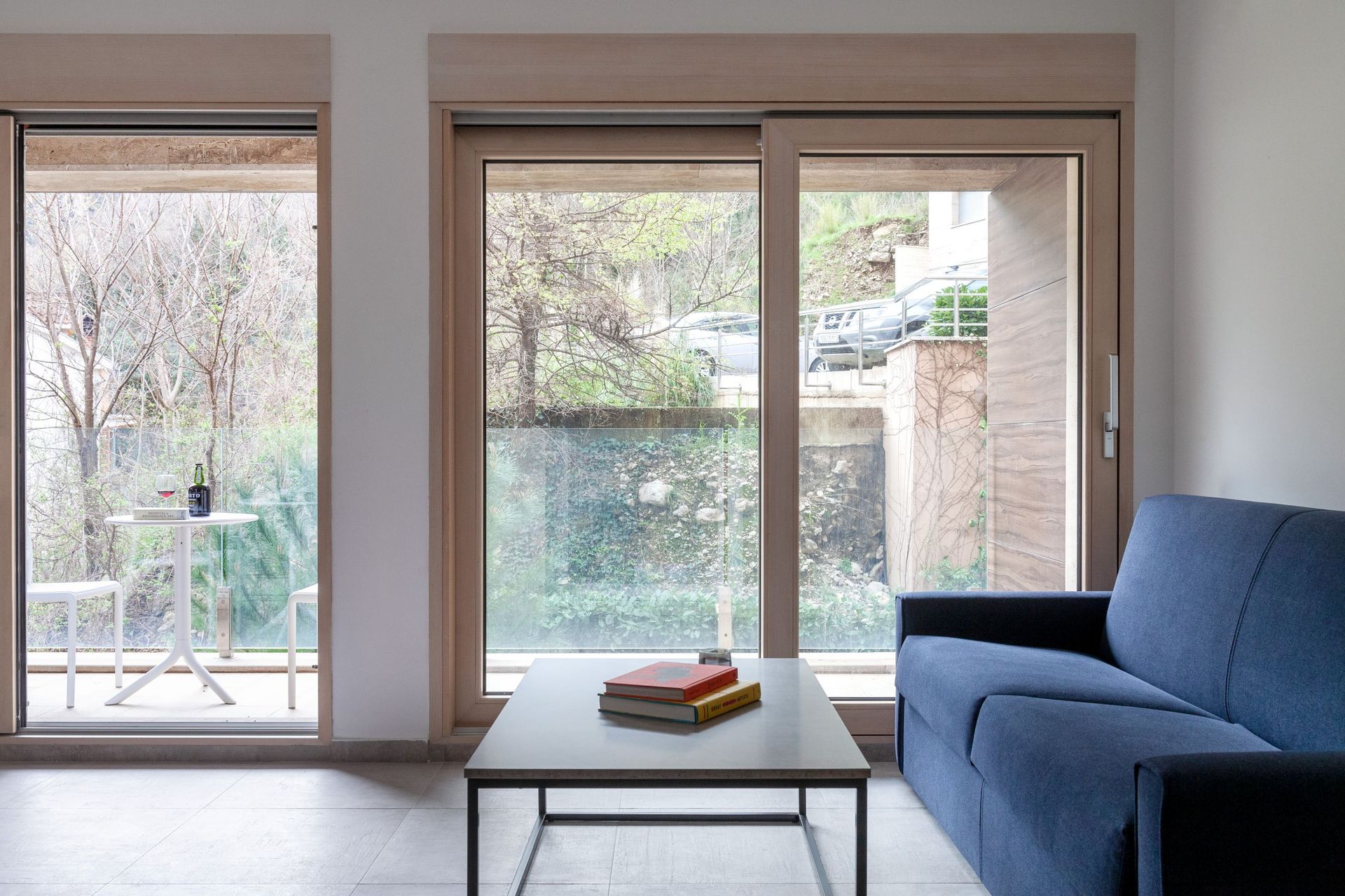Living room with a blue sofa and terrace in a modern apartment in Kotor, Montenegro: panoramic windows and a view of nature.