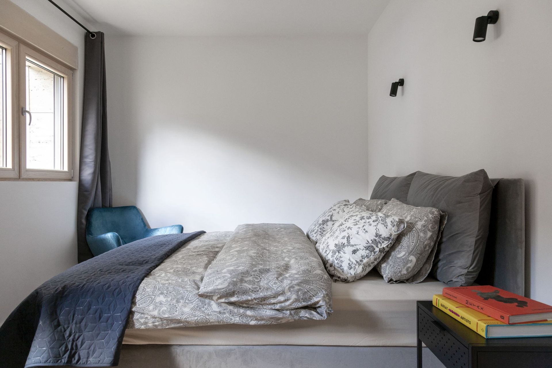 Modern bedroom in an apartment in Kotor, Montenegro: a double bed, a blue armchair, and stylish lighting.