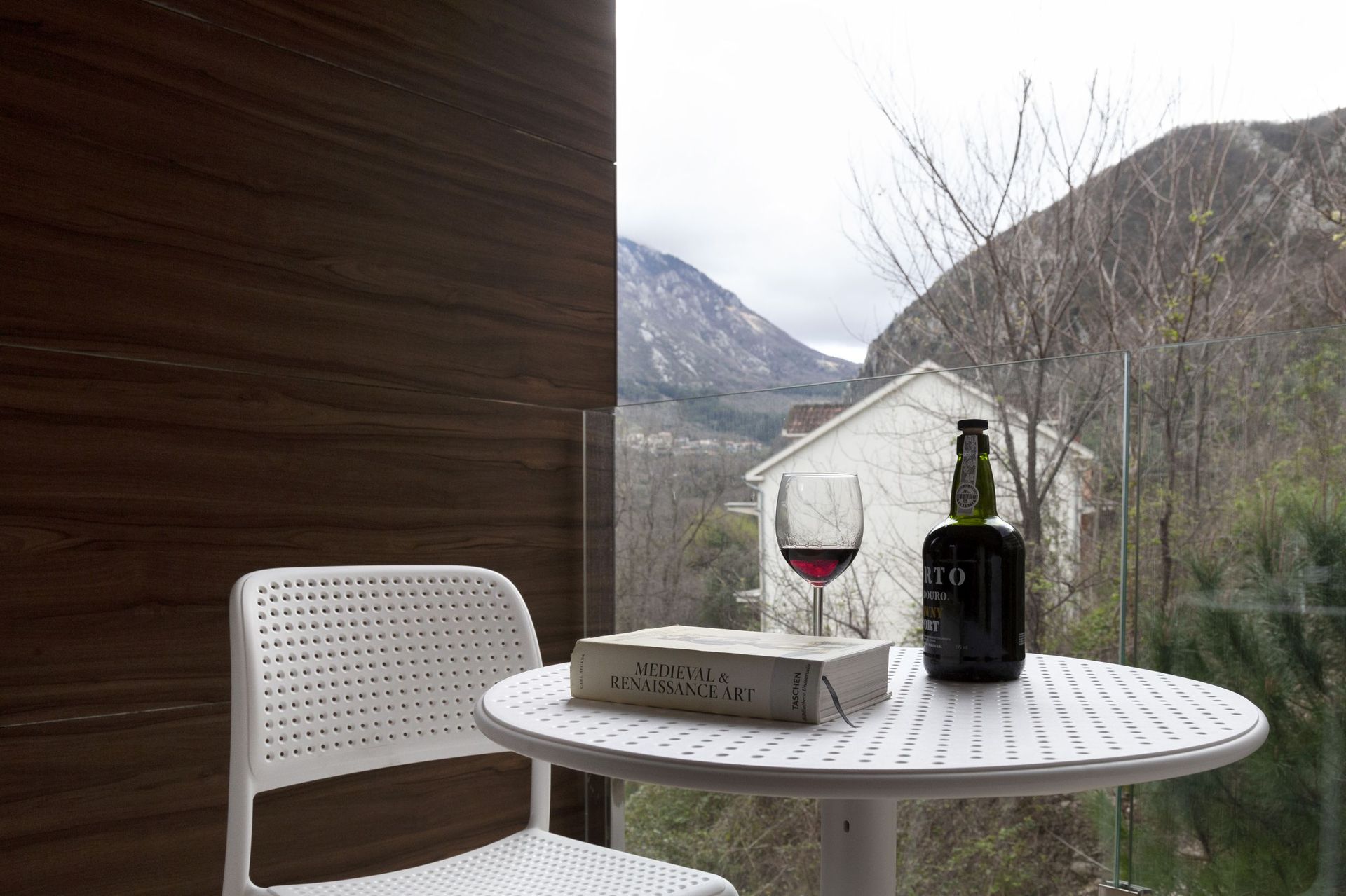 Apartment balcony in Kotor, Montenegro: white table, chair, mountain view, and wood-style wall finish.