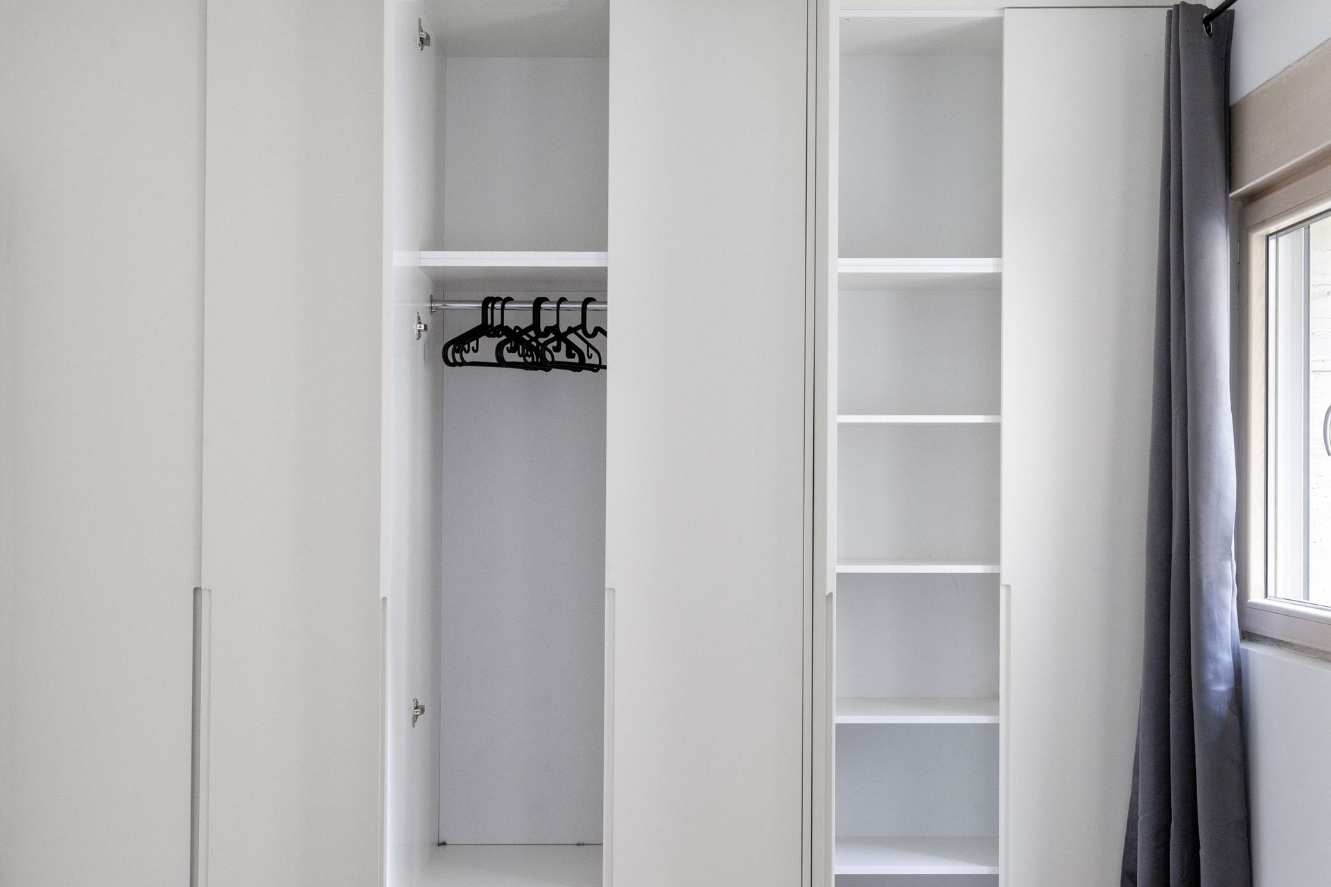 Built-in white wardrobe with shelves and hangers in the bedroom of an apartment in Kotor, Montenegro.