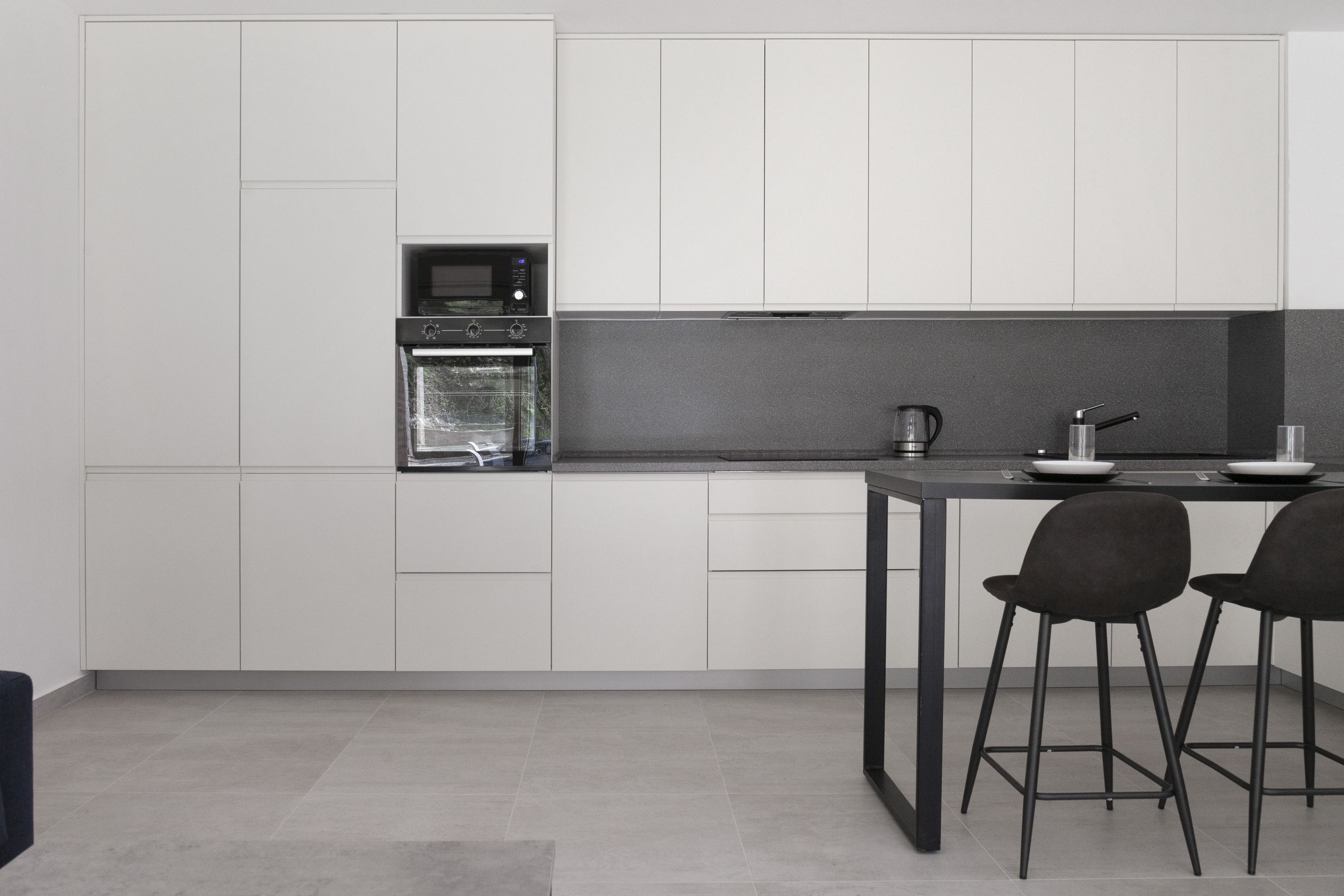 Modern white kitchen with a breakfast bar in an apartment in Kotor, Montenegro: built-in appliances and a gray backsplash.