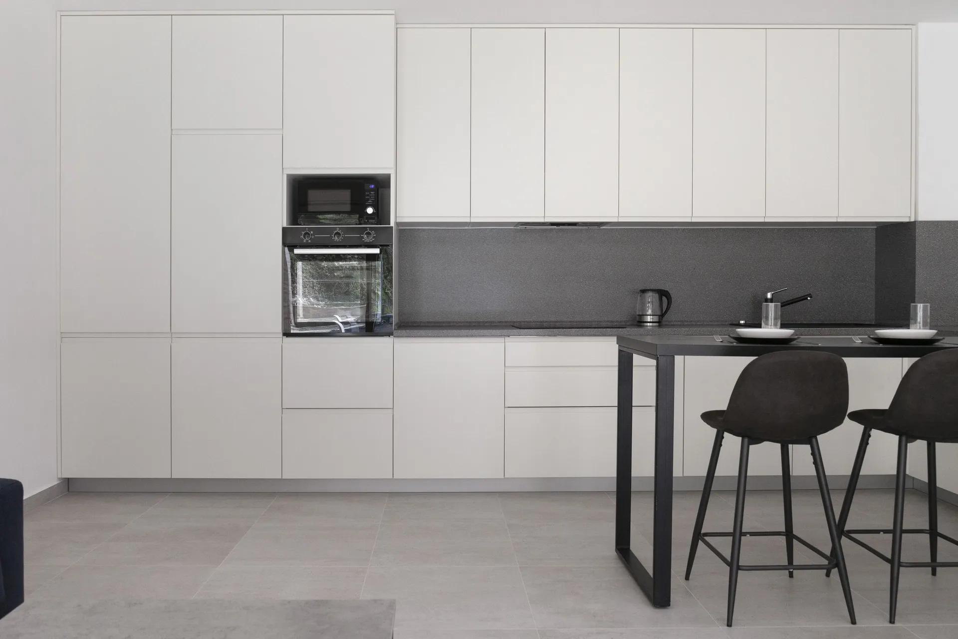 Modern kitchen featuring white glossy cabinets, a dark countertop, built-in appliances, and a black bar table with stools.