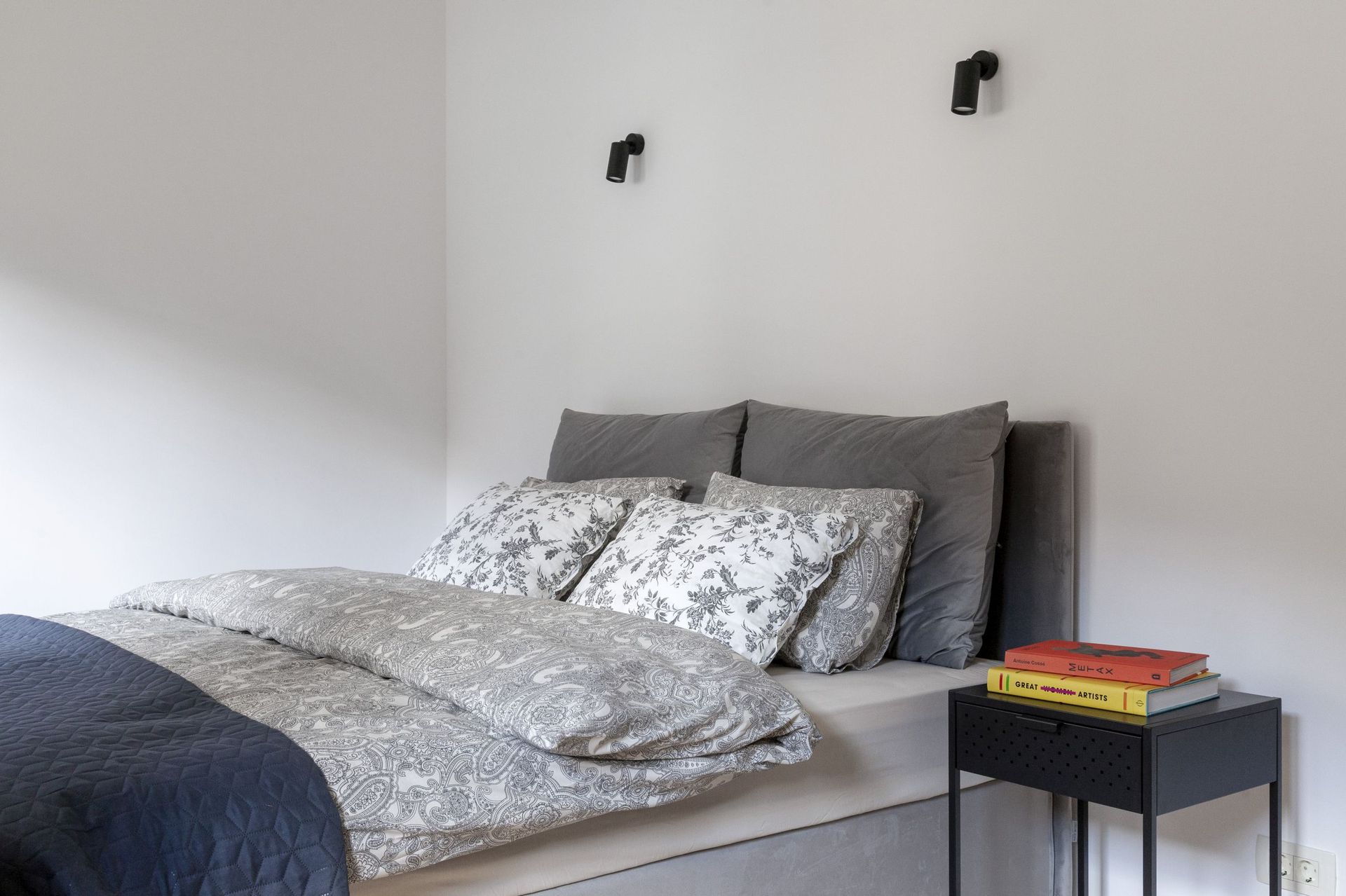 Cozy bedroom in an apartment in Kotor, Montenegro: a double bed with gray textiles and black bedside tables.