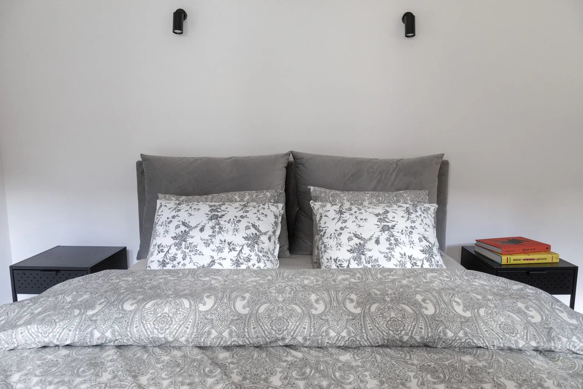 Modern bedroom featuring a double bed with a grey headboard and white pillows decorated with a floral pattern.
