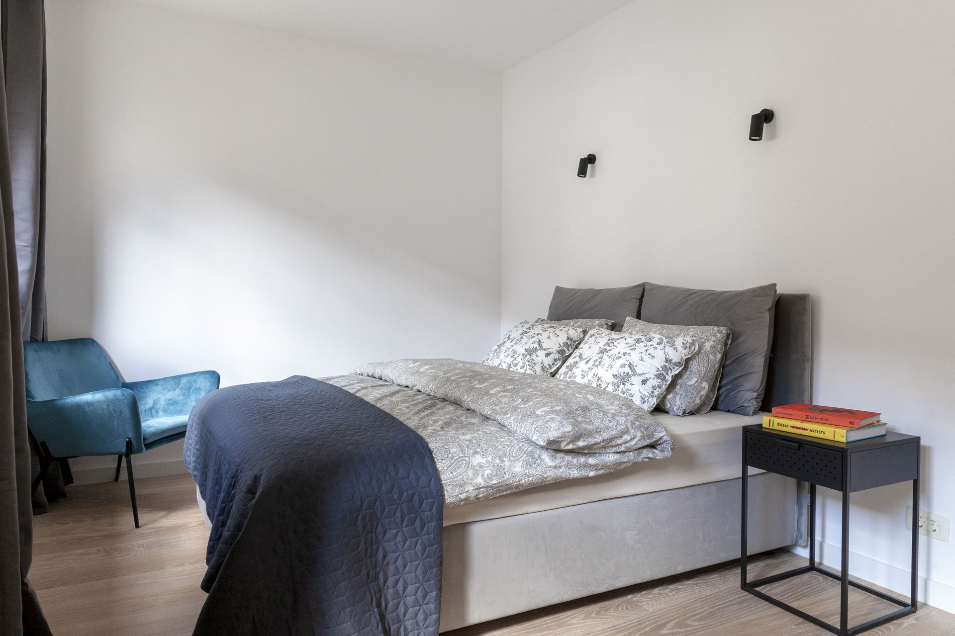 Modern bedroom in an apartment in Kotor, Montenegro: a double bed, a blue armchair, and stylish wall sconces.
