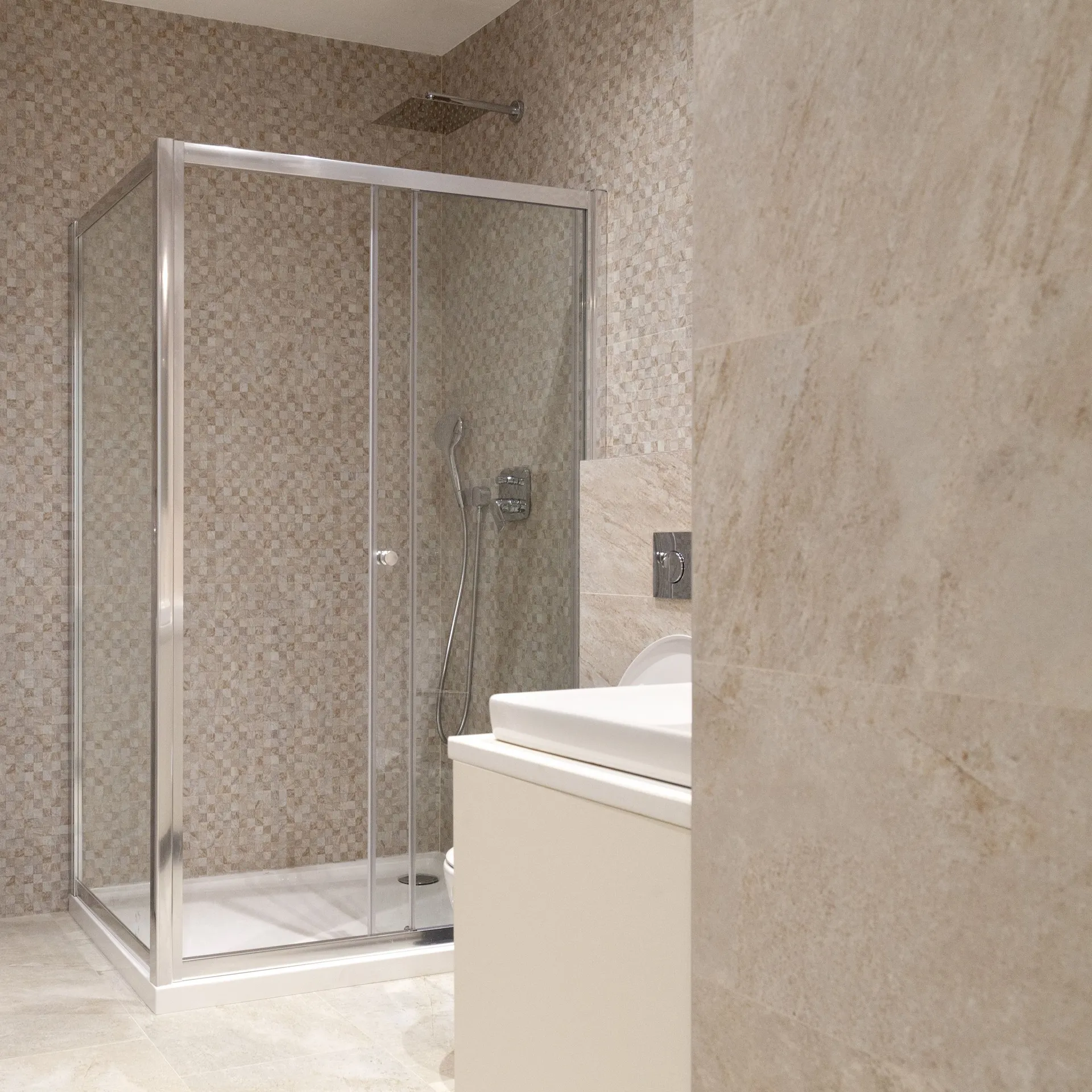 Modern bathroom featuring a glass shower enclosure with mosaic tiles and a white vanity sink unit.