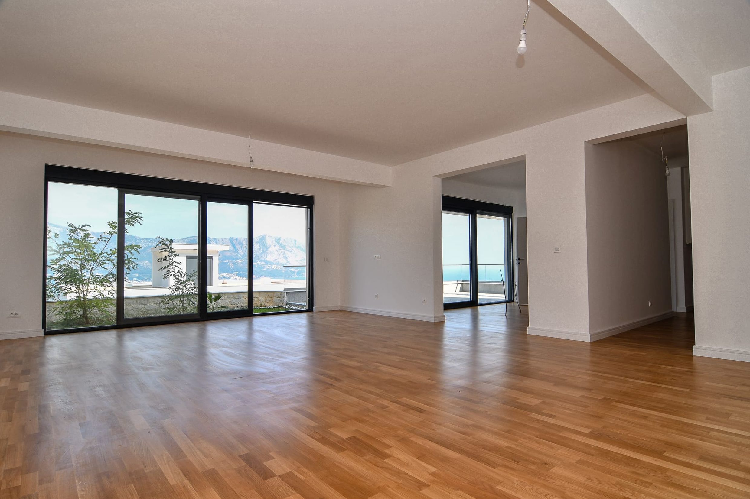 Spacious living room with panoramic windows and sea view in a new villa in Budva, Montenegro, parquet flooring.