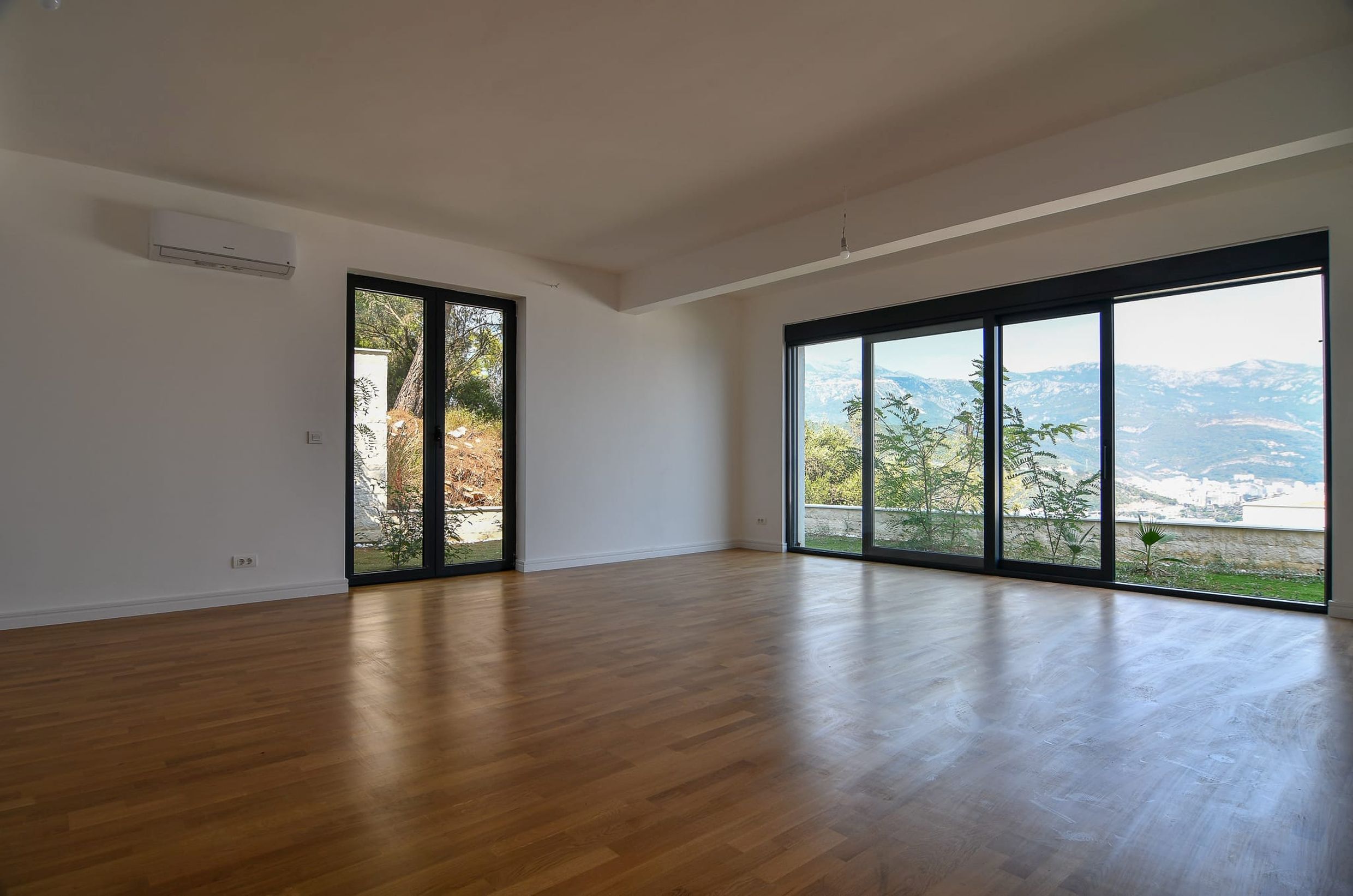 Bright living room with panoramic windows and mountain views in a villa in Budva, Montenegro: parquet flooring and modern finishes.