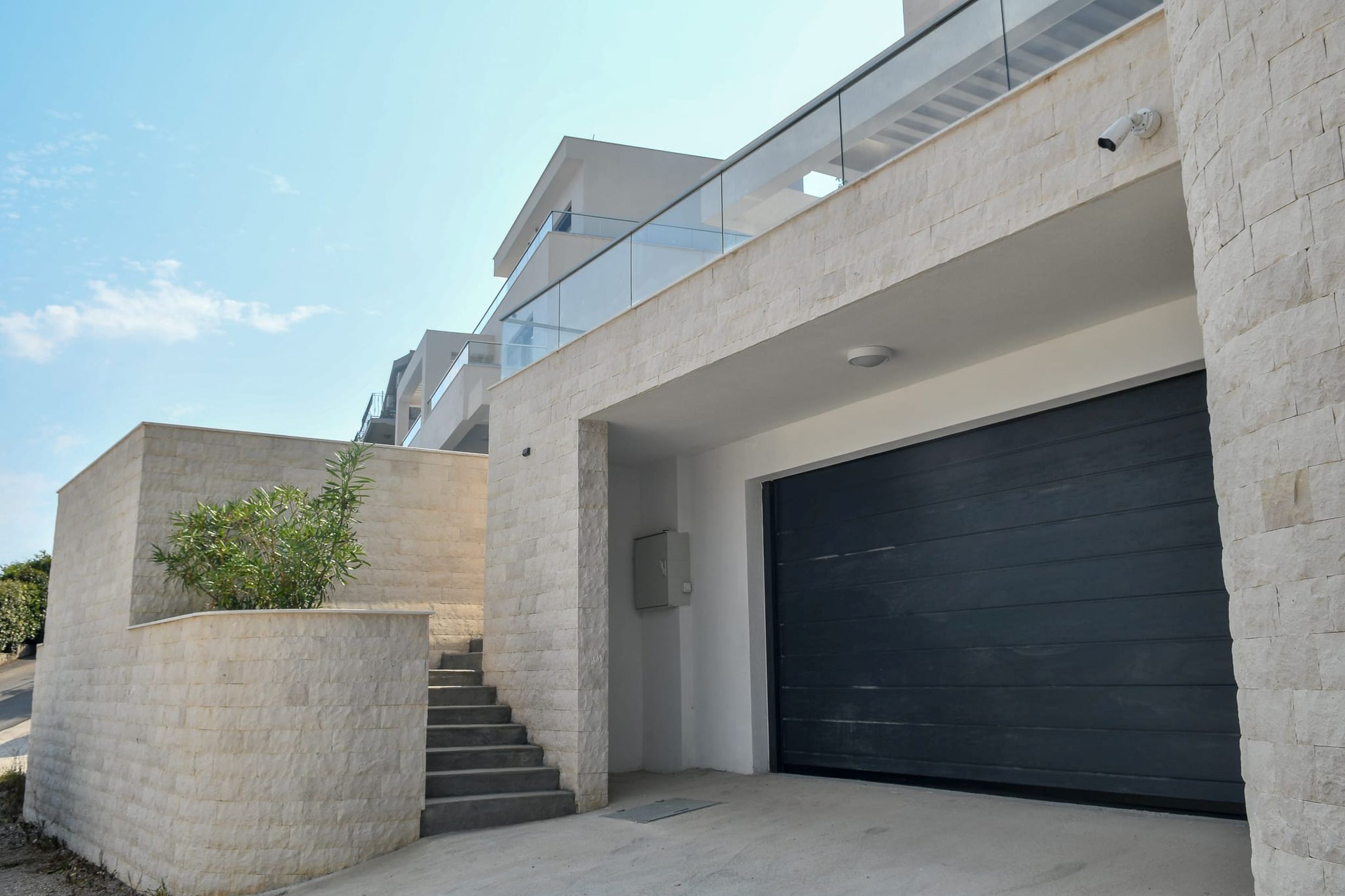Modern villa in Budva, Montenegro: stone-clad facade, garage doors, and staircase to the terrace.