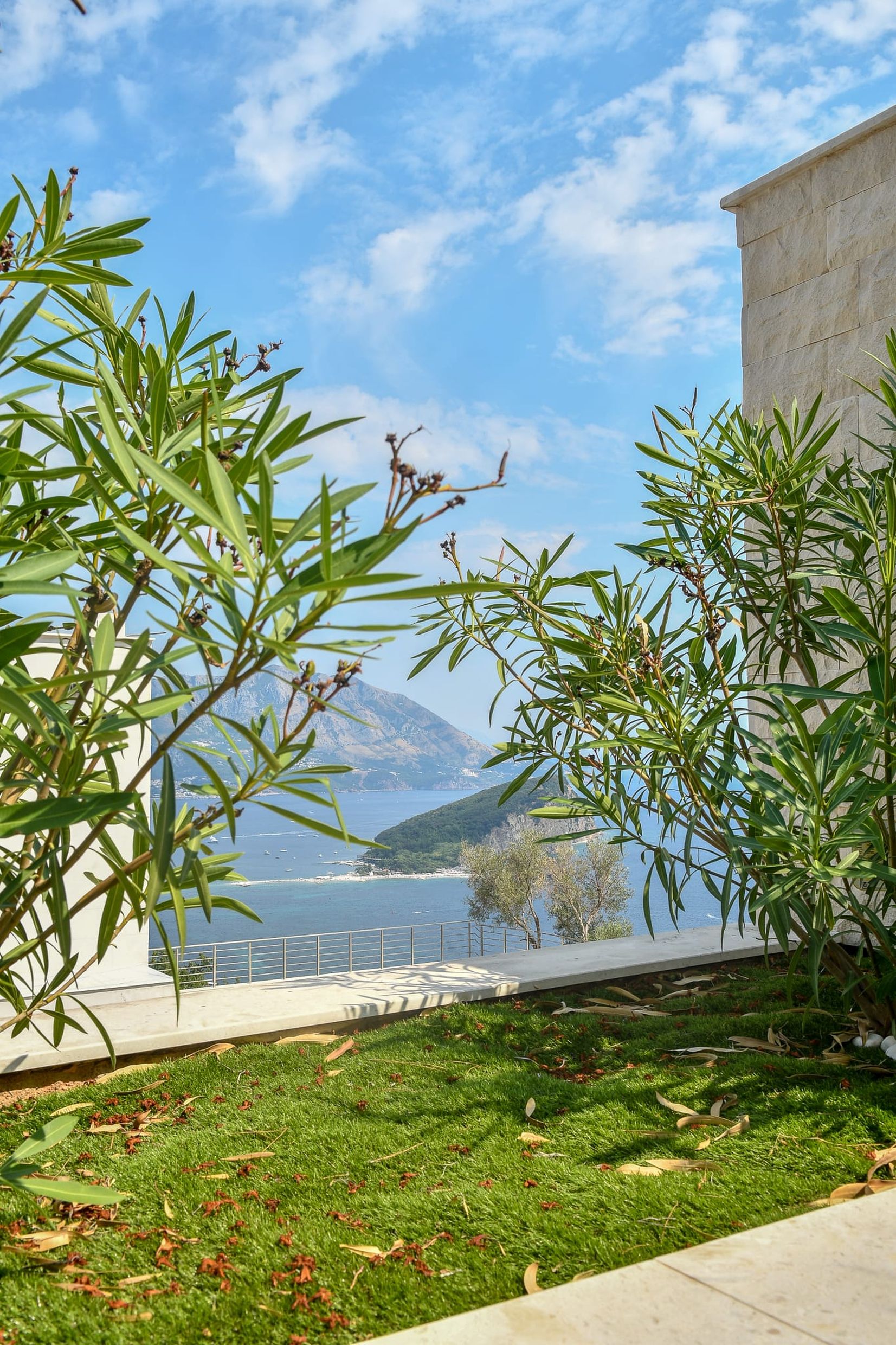 View from the villa terrace in Budva, Montenegro: a panorama of the sea, St. Nicholas Island, and the mountains through the garden greenery.
