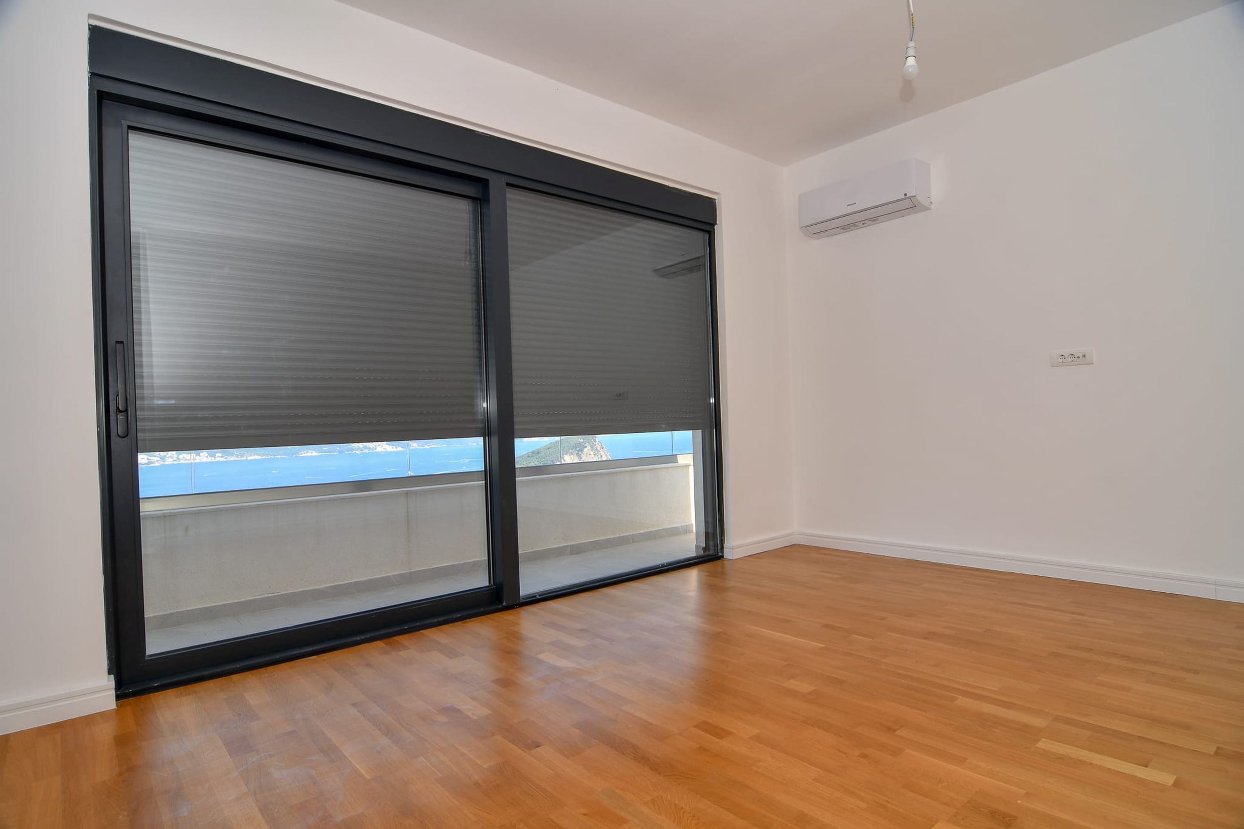 Bright living room with a panoramic window, sea view, and terrace in a villa in Budva, Montenegro. Parquet flooring and air conditioning.
