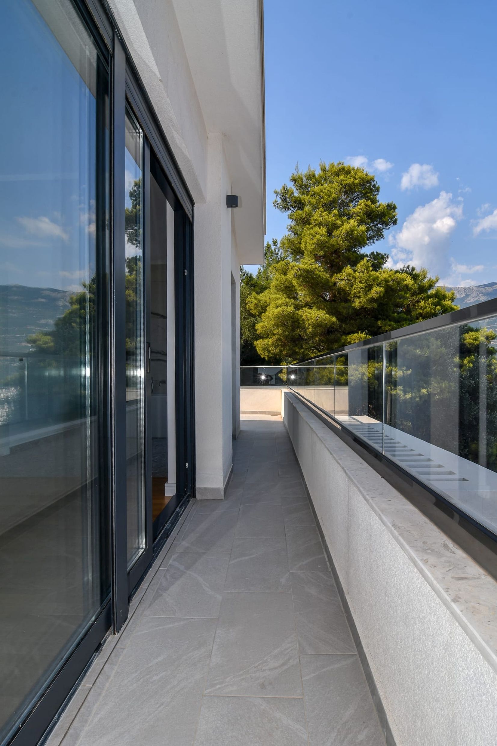 Spacious villa balcony in Budva, Montenegro, with panoramic glazing, glass railing, and a view of greenery.