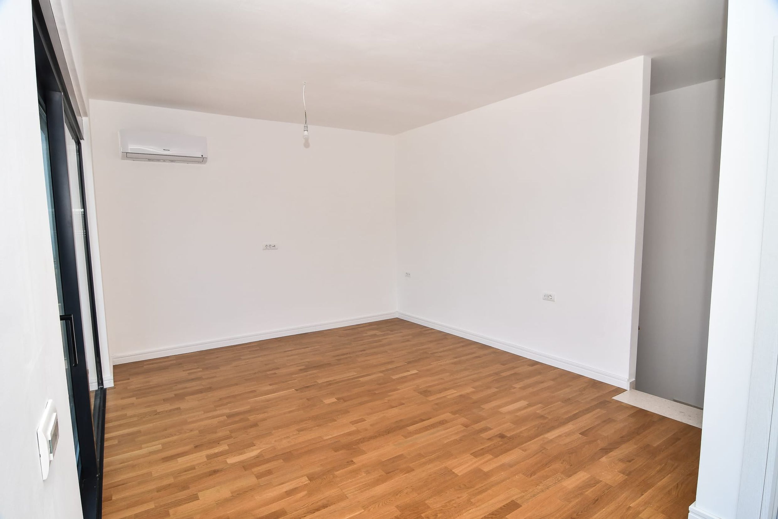Bright living room with parquet flooring and air conditioning in a new villa in Budva, Montenegro. Empty room with white finishes.