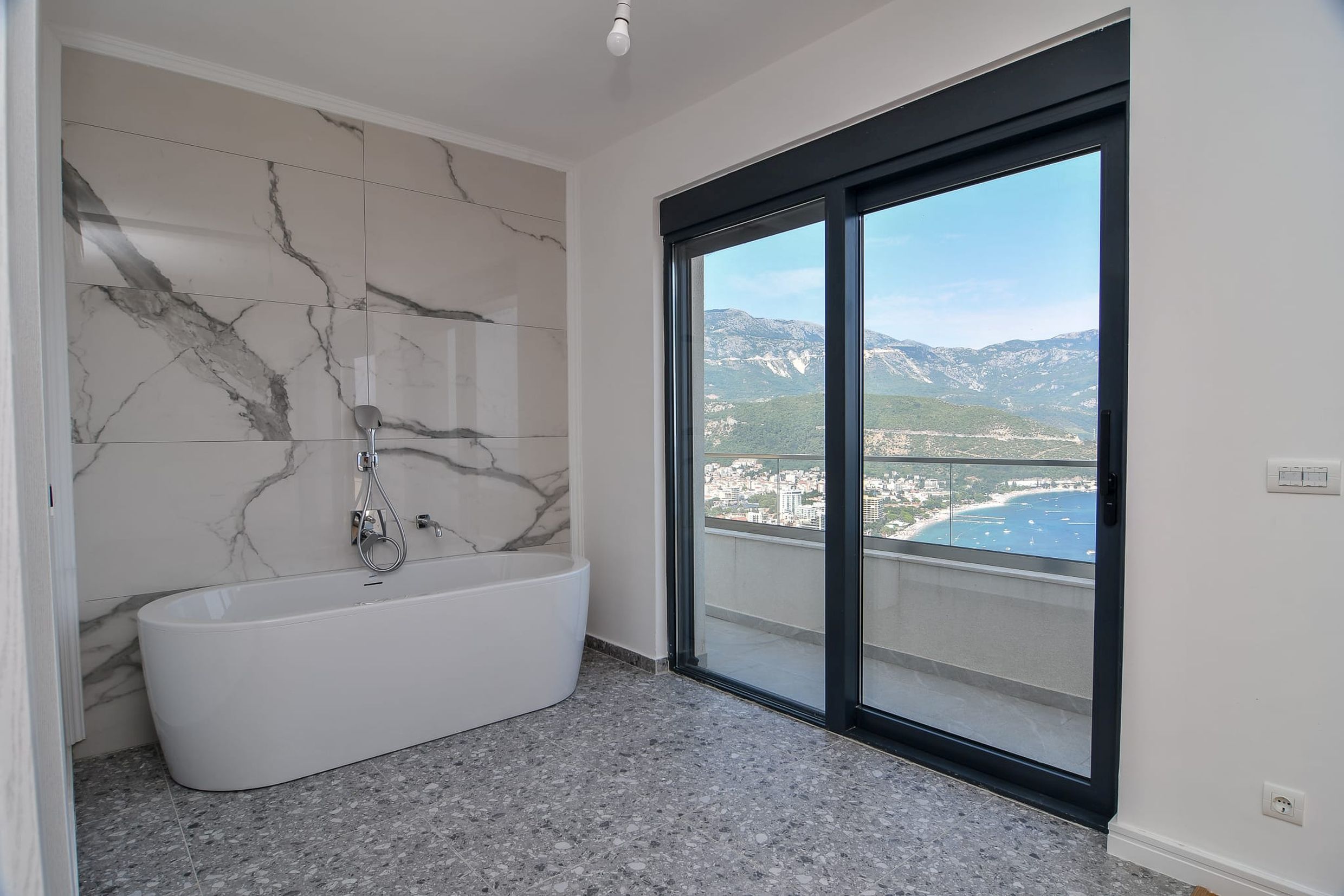 Bathroom with panoramic sea and mountain views in a villa, Budva, Montenegro: freestanding bathtub and marble-look tiles.