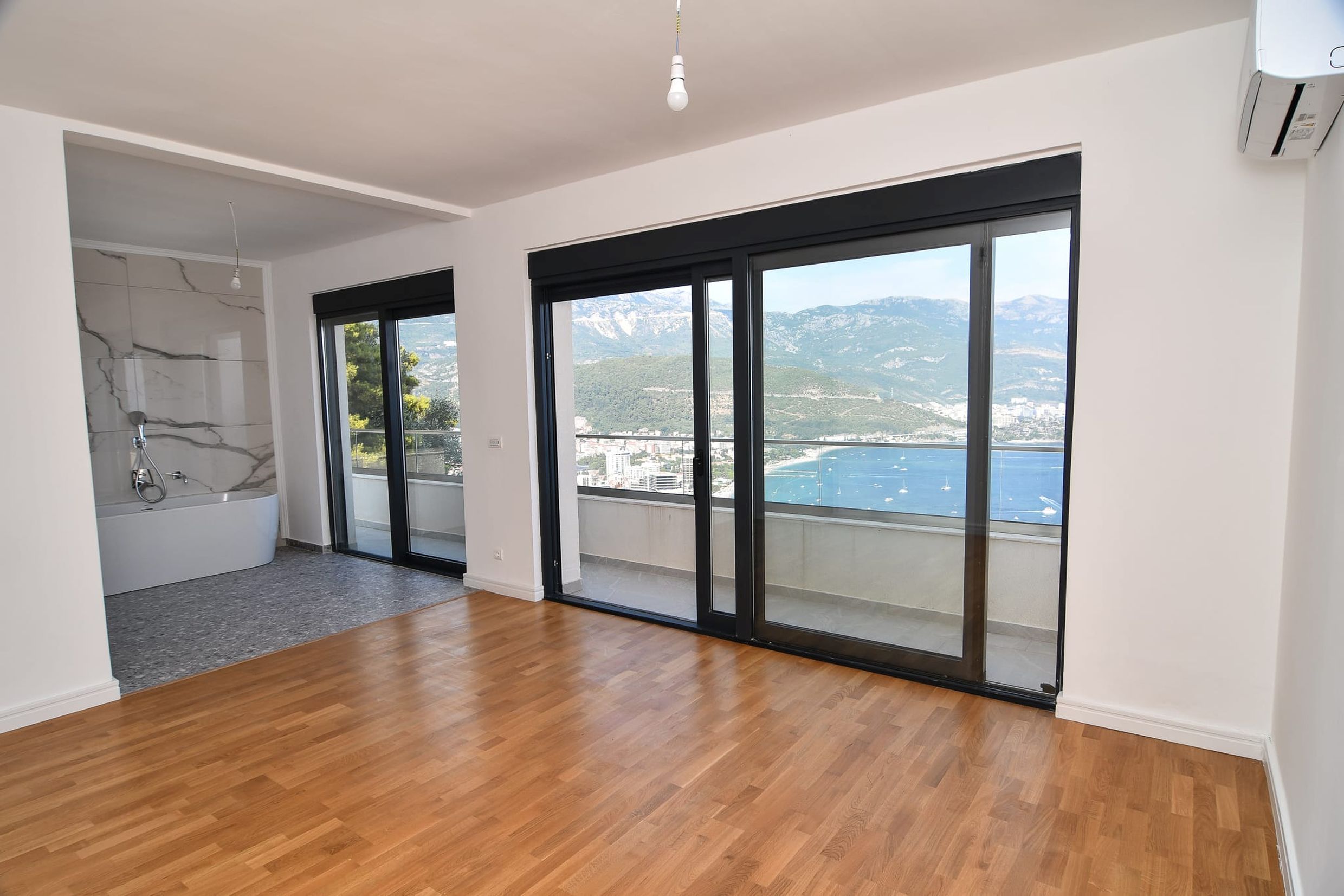 Living room with panoramic sea and mountain views in a villa in Budva, Montenegro, with a bathtub by the window and parquet flooring.