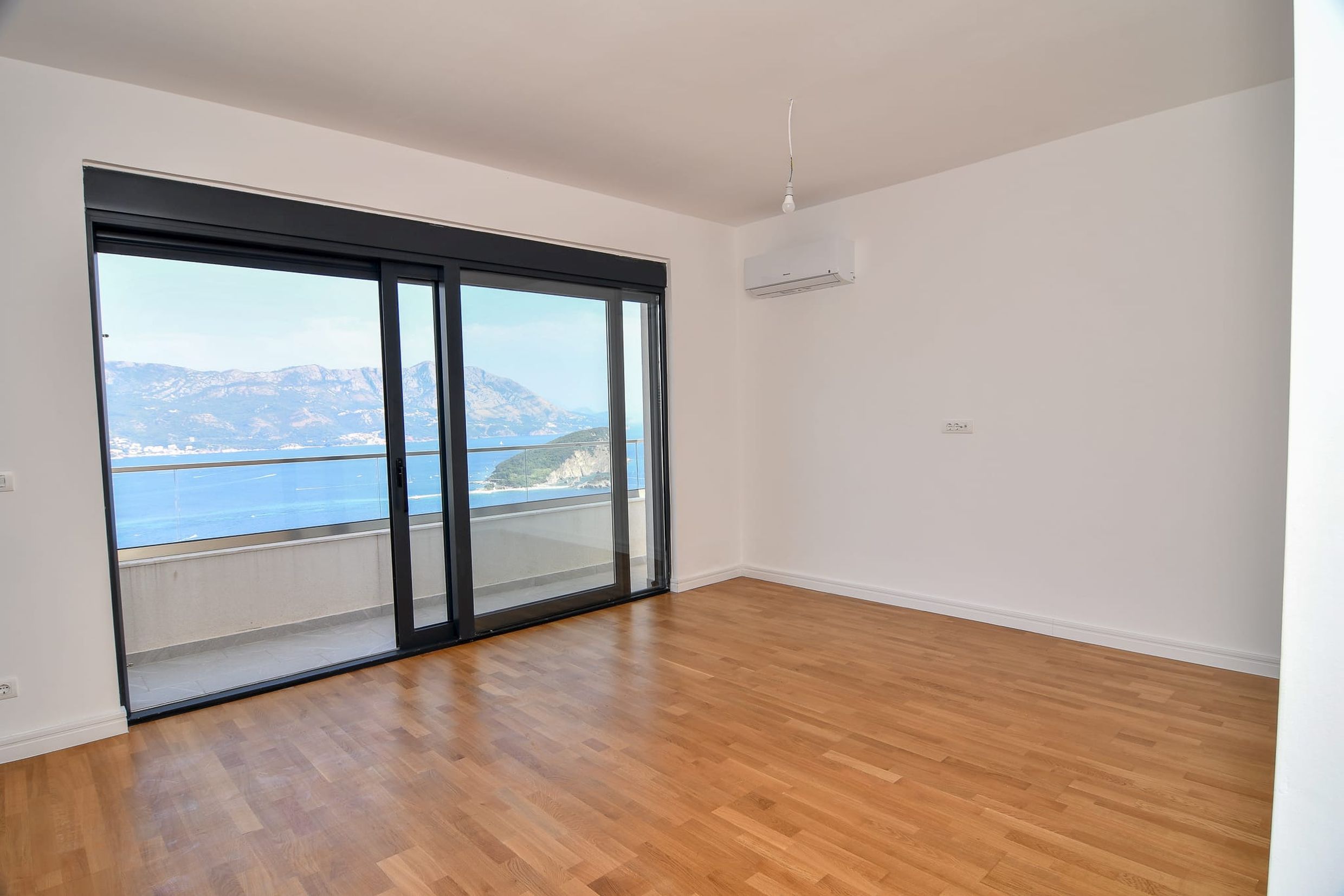 Bright living room with panoramic sea and mountain views in a villa in Budva, Montenegro: parquet flooring, balcony, and air conditioning.