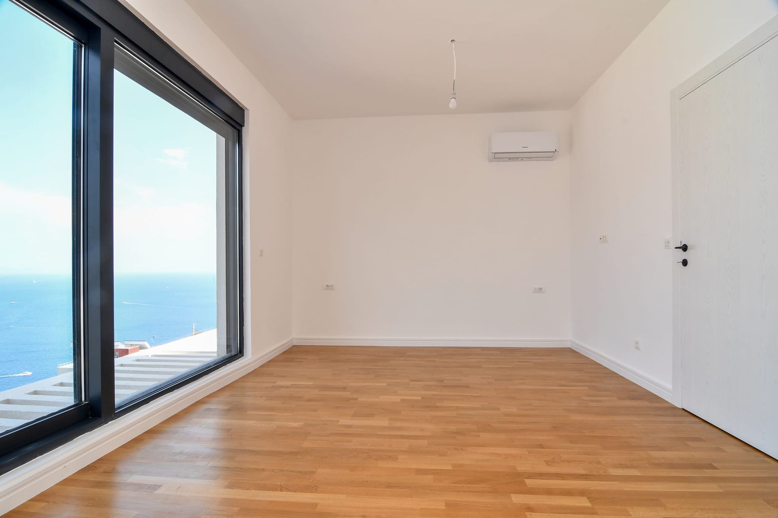 Empty bedroom with panoramic sea view in a villa, Budva, Montenegro: light finishes, parquet flooring, and air conditioning.