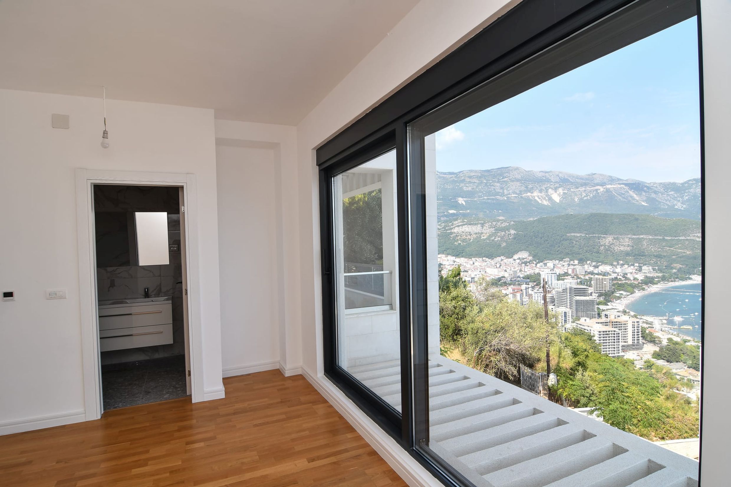 Bedroom with a panoramic window and views of the sea and mountains in a villa, Budva, Montenegro. Modern interior with parquet flooring.