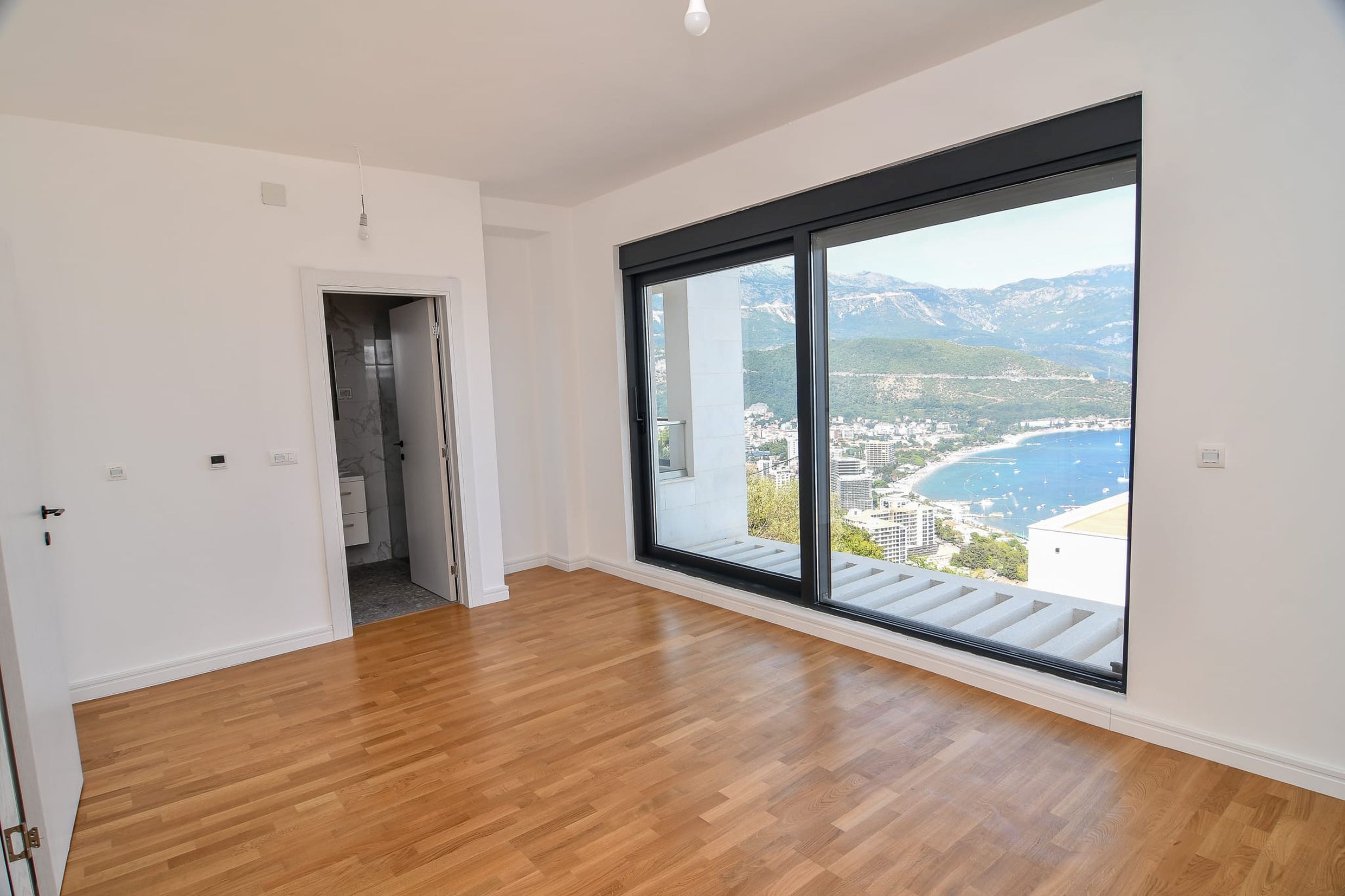 Bright living room with panoramic sea and mountain views in a villa, Budva, Montenegro: parquet floor and access to the terrace.