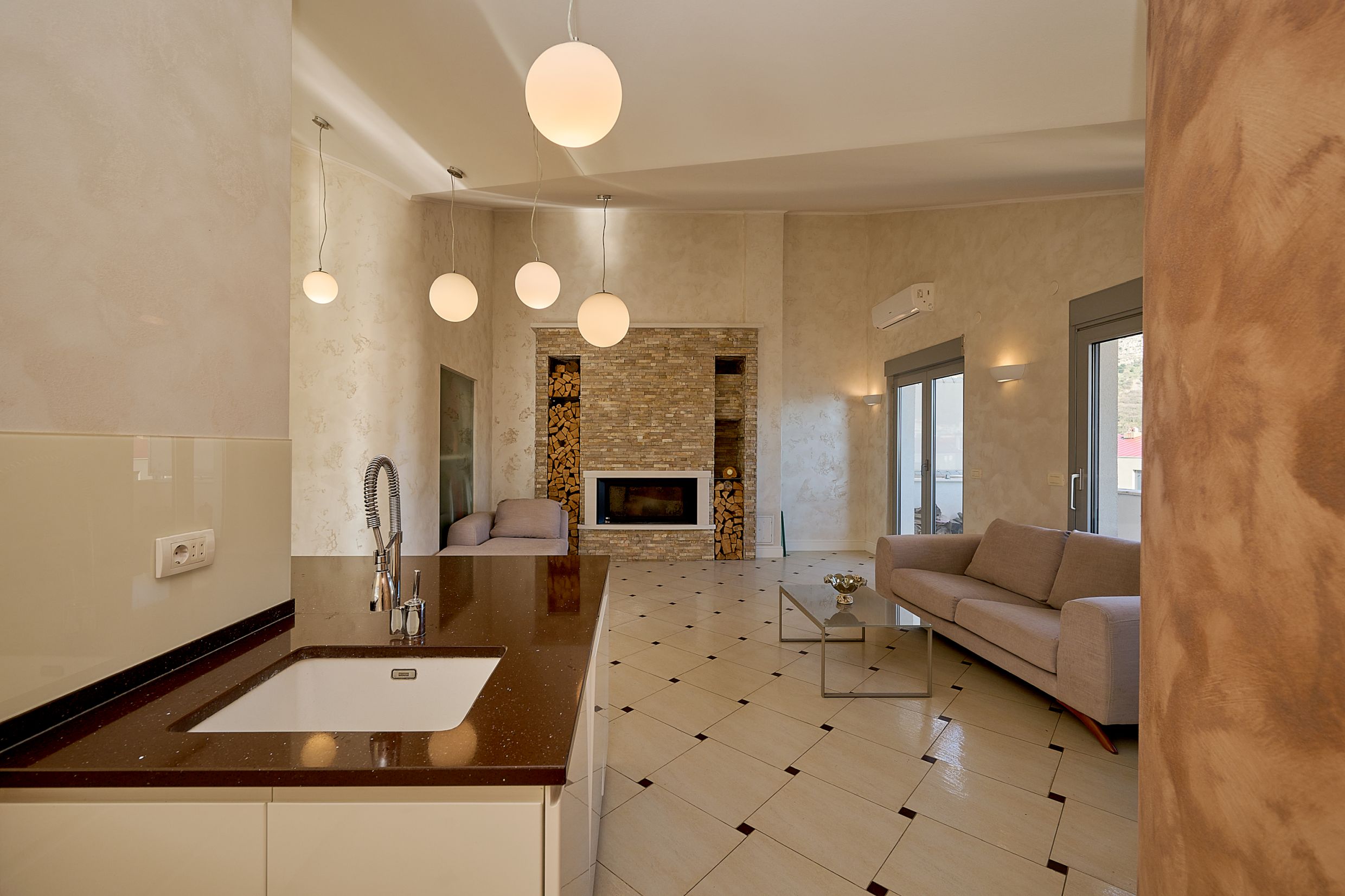 Living room with fireplace and kitchen in an apartment in Budva, Montenegro: modern furniture, light finishes, and tiled flooring.