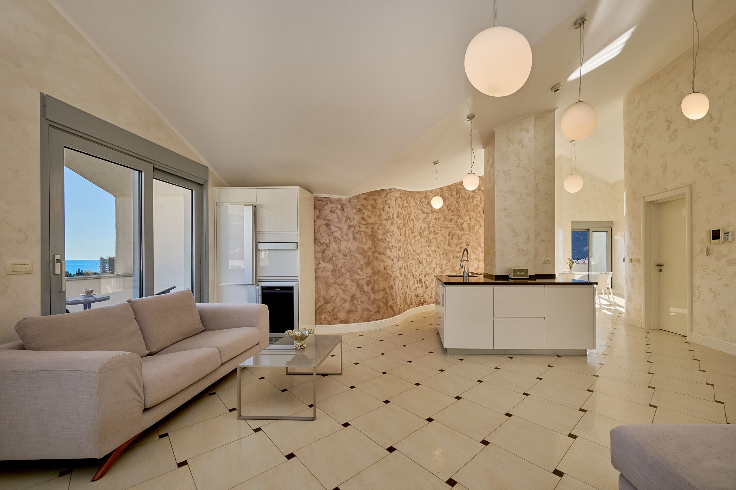 Modern living room with an island kitchen and sea view in an apartment, Budva, Montenegro. Bright interior, tile flooring.