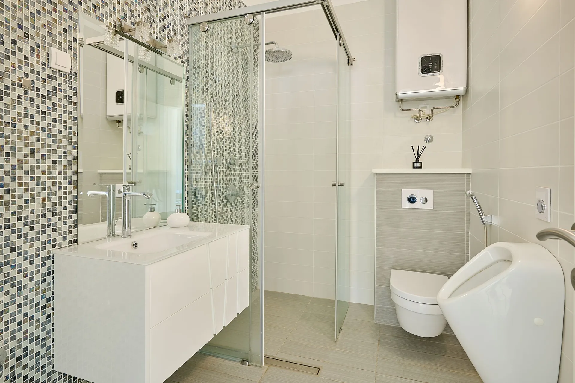Modern bathroom with mosaic wall, glass shower enclosure, white vanity sink, and toilet fixtures.