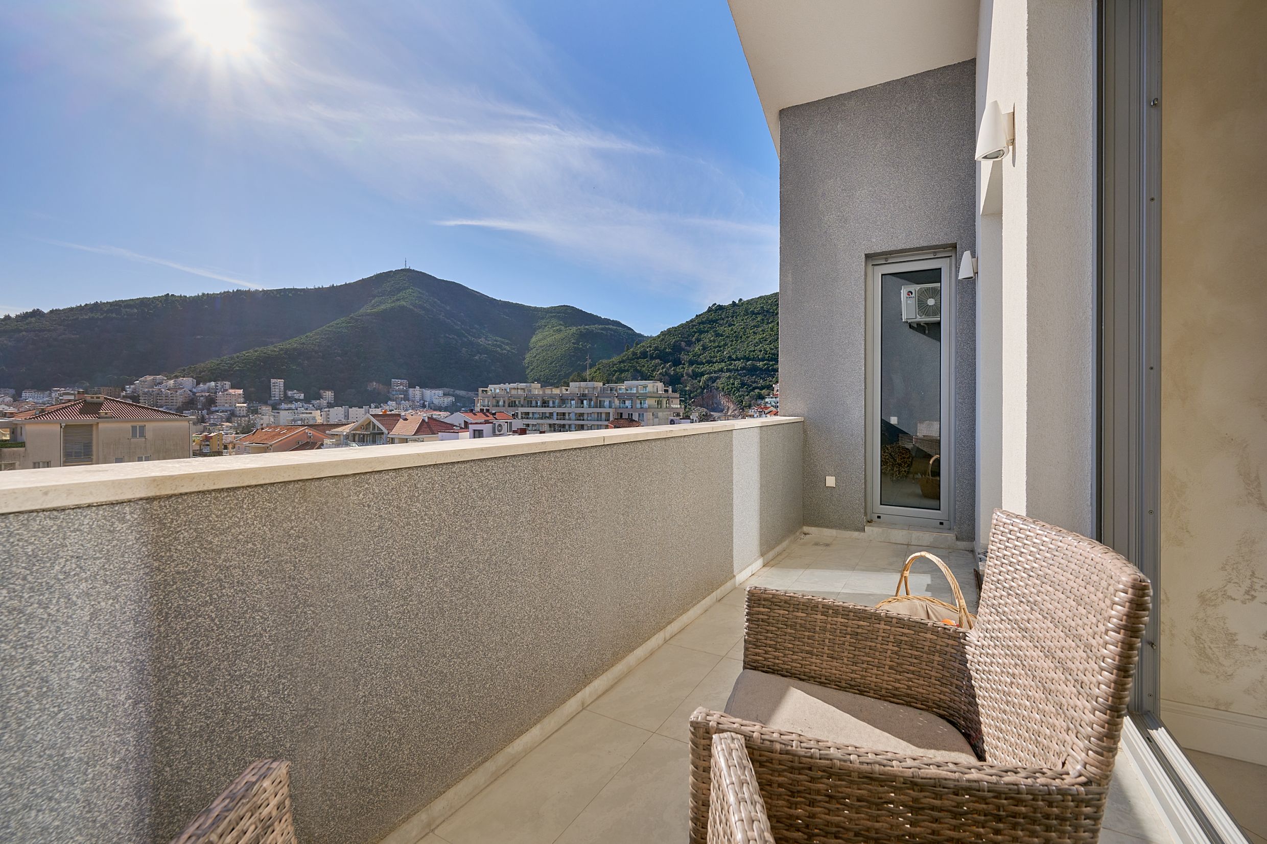 Spacious balcony with wicker furniture and panoramic views of the mountains and the city of Budva, Montenegro.