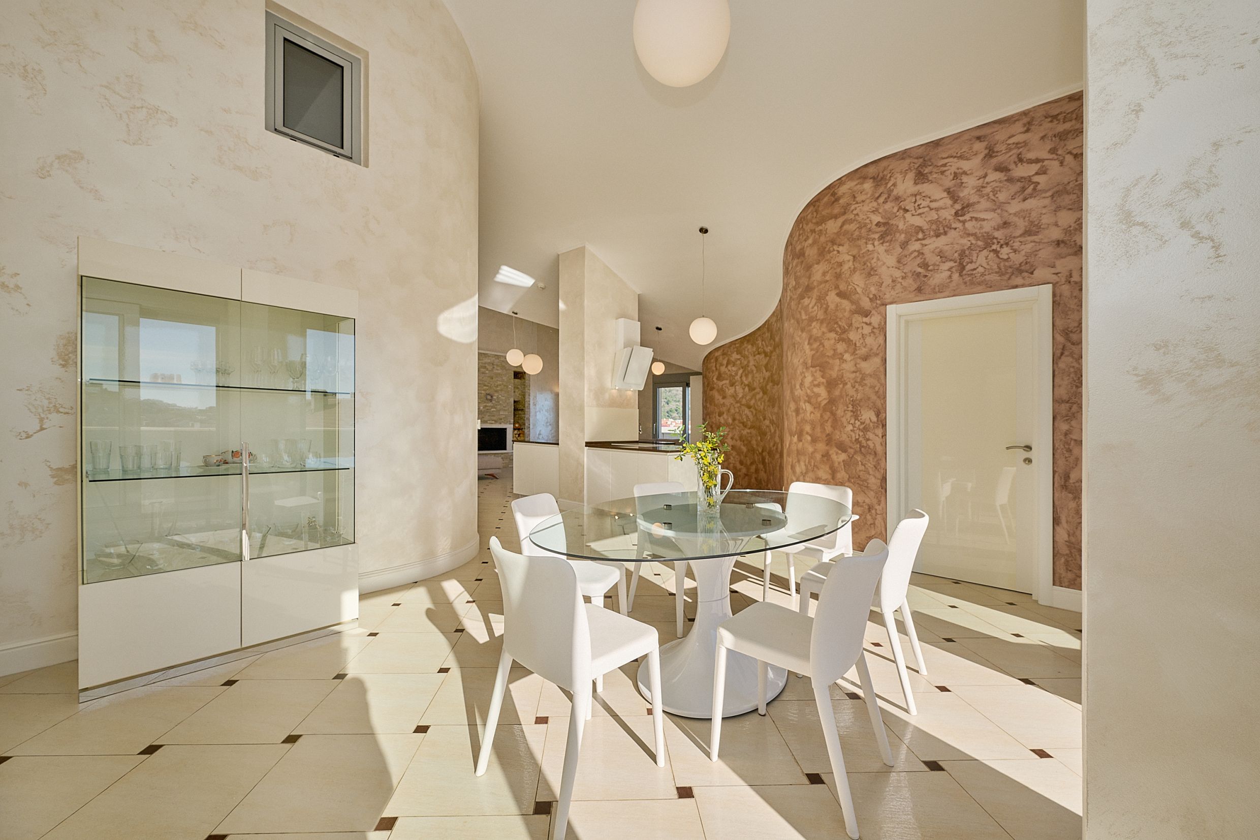Modern living room with dining area in an apartment, Budva, Montenegro: glass table, white chairs, and wall decor.