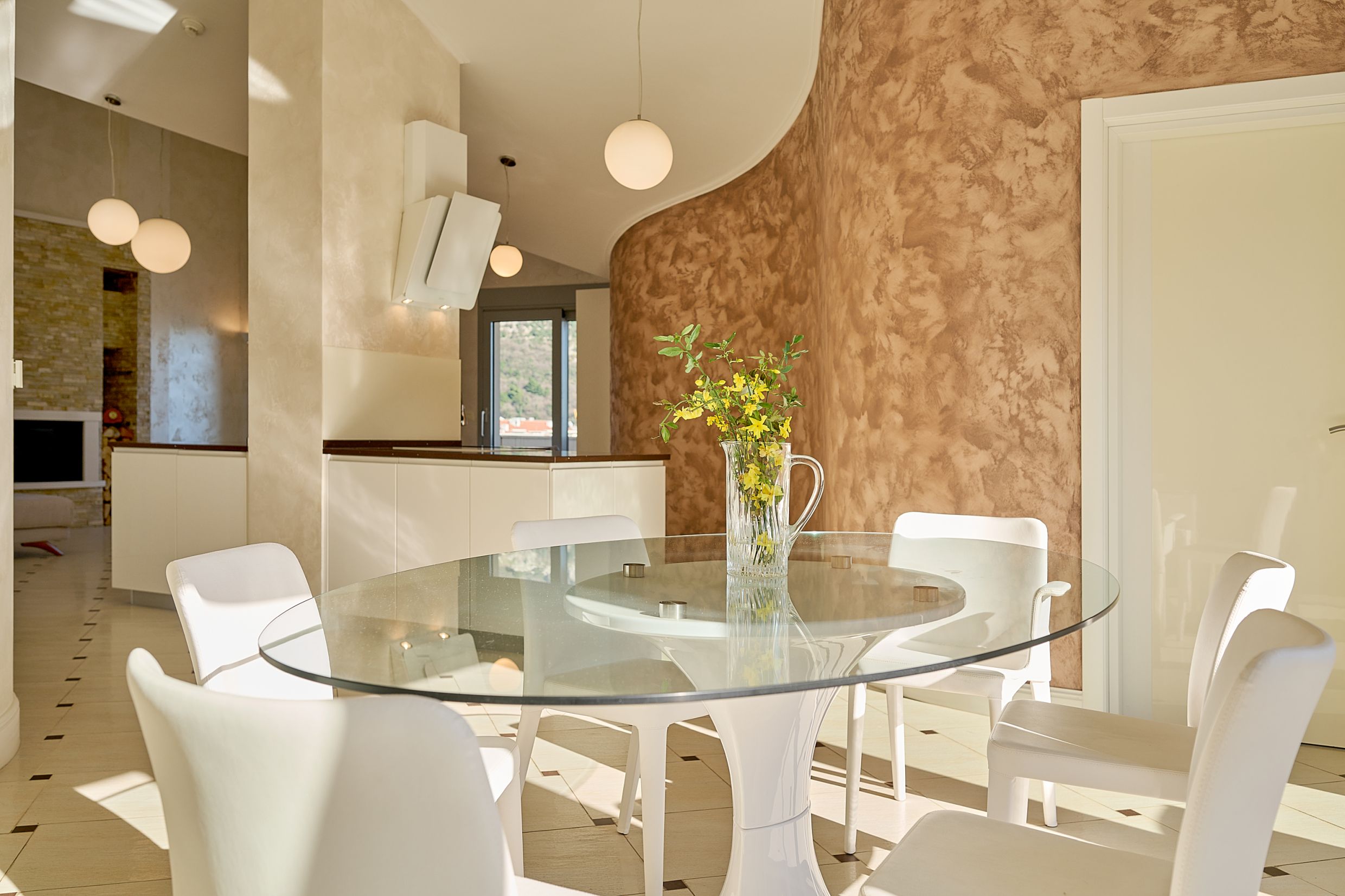 Modern living room with dining area in an apartment in Budva, Montenegro: glass table, white chairs, and wall decor.