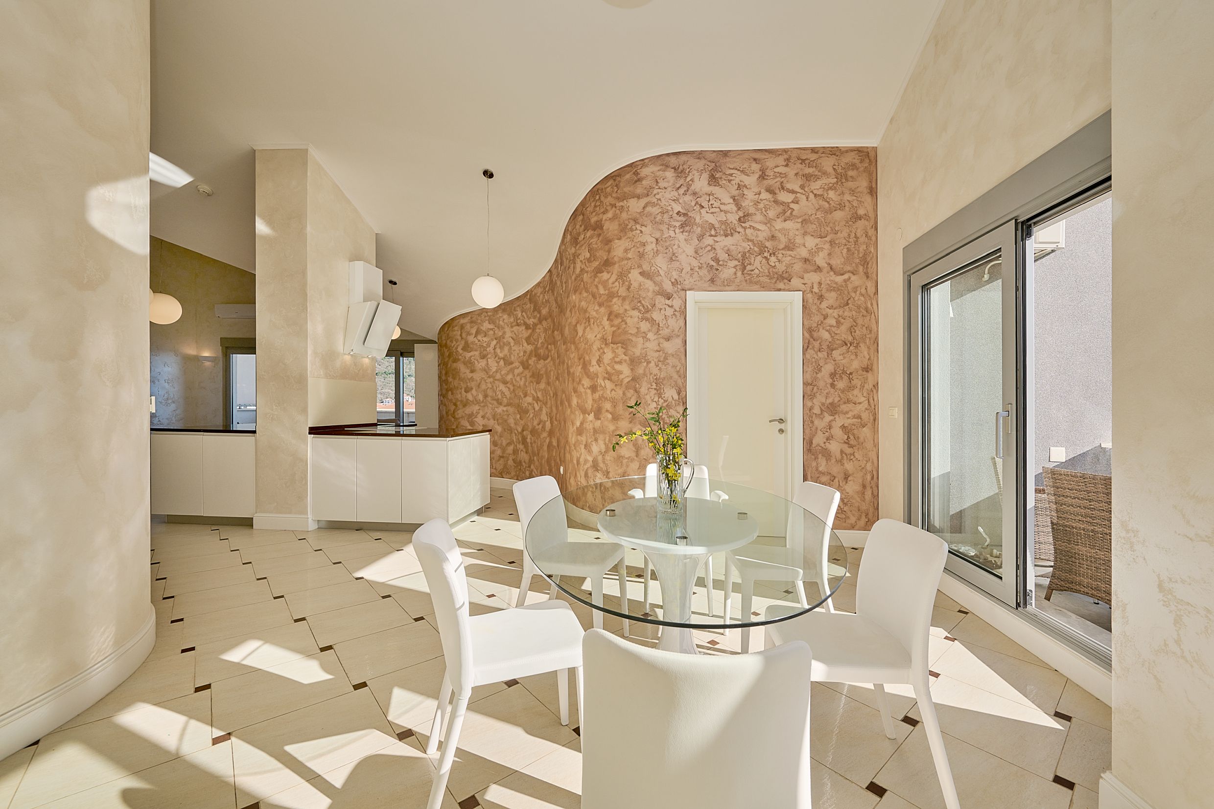 Bright living room with dining area and kitchen in an apartment in Budva, Montenegro: glass table, white chairs, and decor.