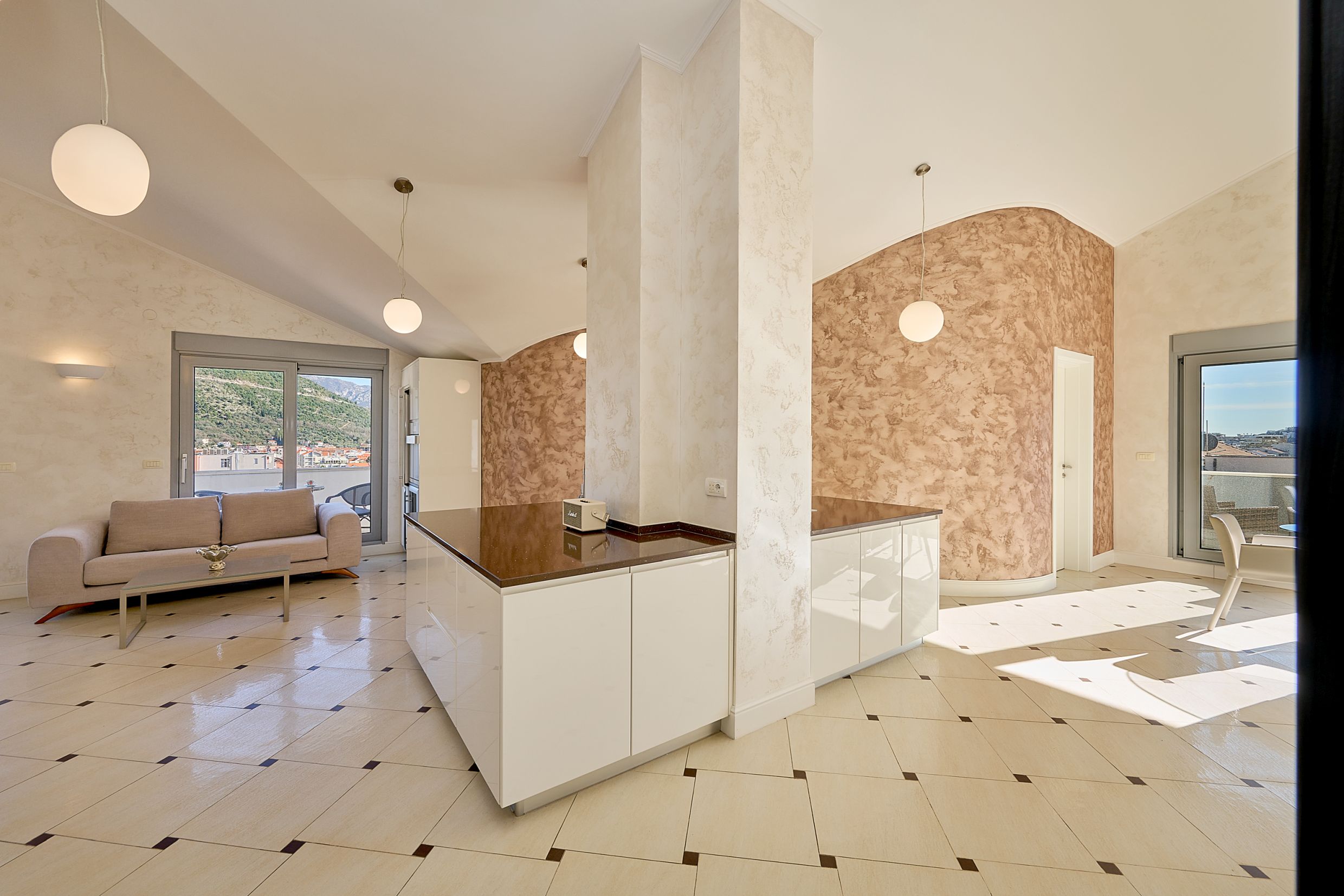 Modern kitchen-living room in an apartment in Budva, Montenegro: glossy fronts, decorative plaster, and mountain views.