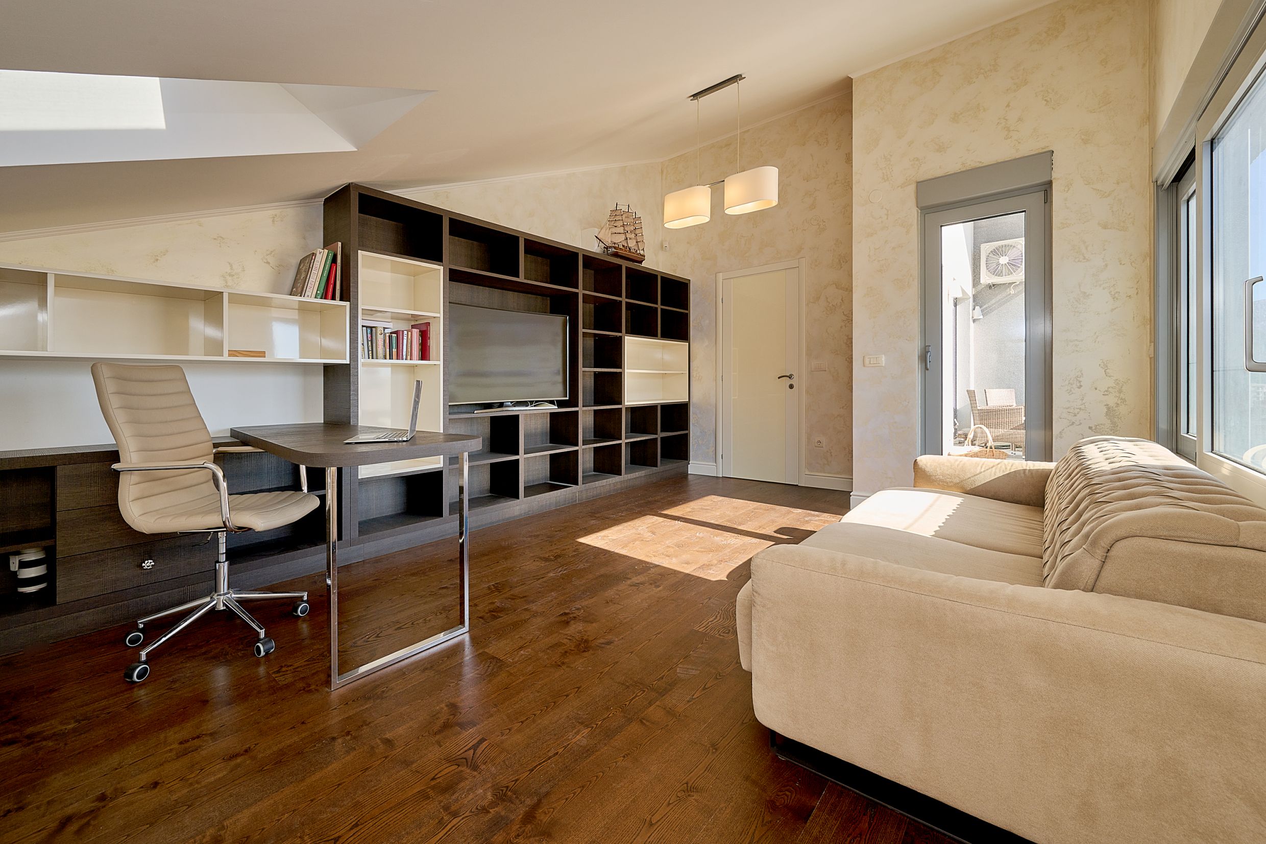 Living room with a workspace in an apartment in Budva, Montenegro: modern furniture, shelving unit, sofa, and access to the terrace.