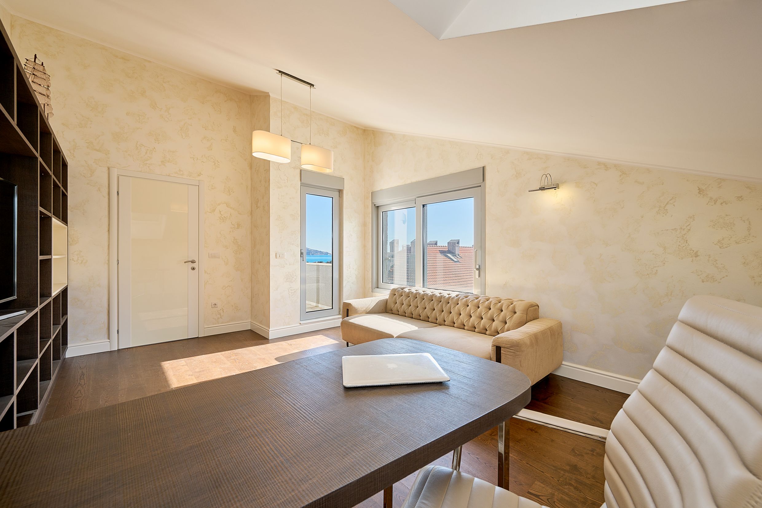 Living room with a beige sofa, desk, and sea view in an apartment in Budva, Montenegro. Modern interior.