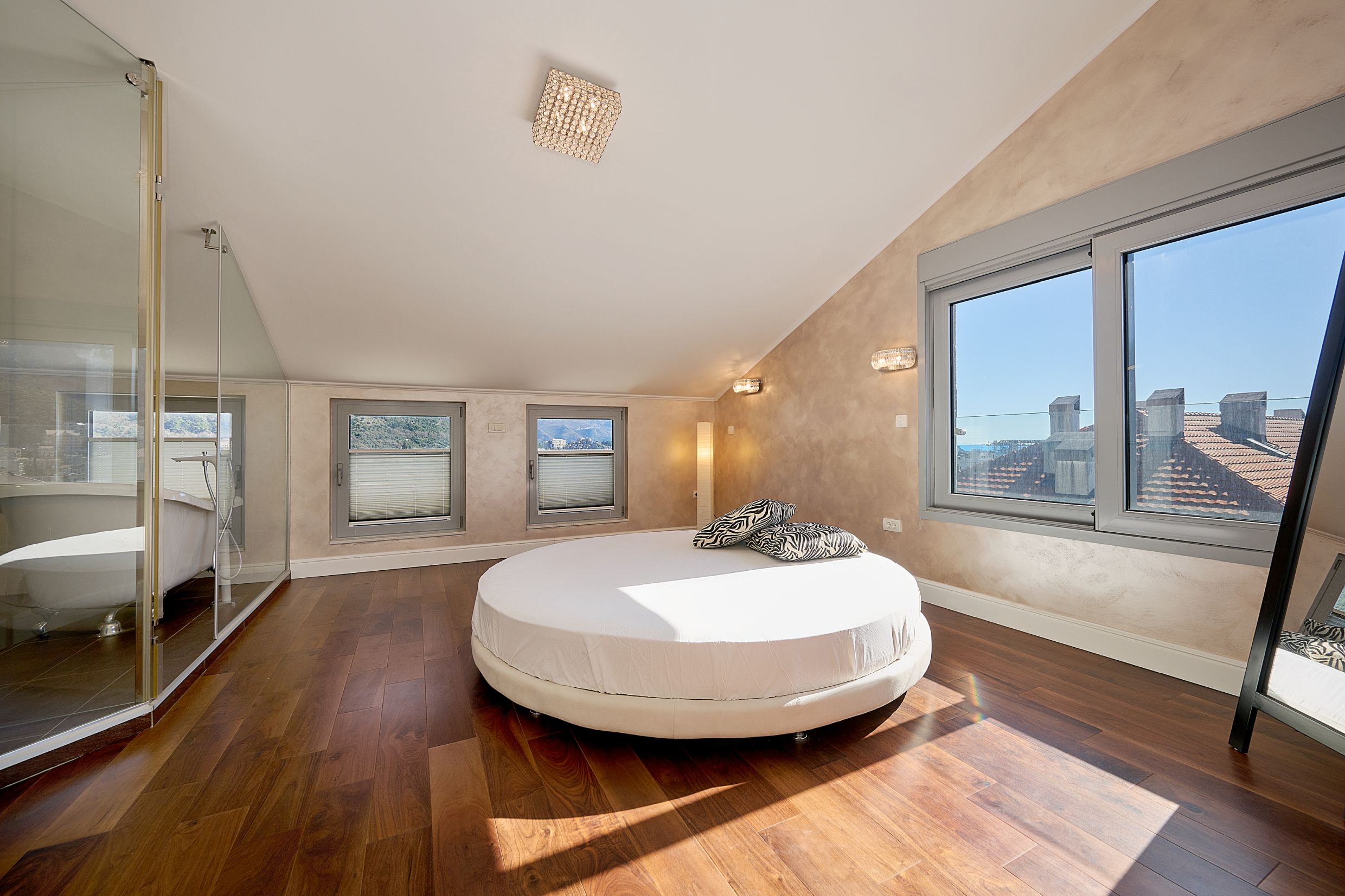 Bedroom with a round bed, glass bathtub, and sea view in an apartment in Budva, Montenegro. Modern interior.