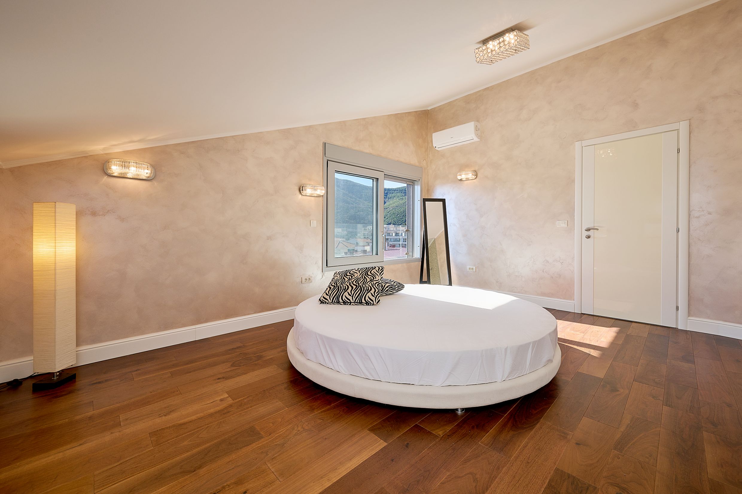 Bedroom with a round bed and mountain view in an apartment, Budva, Montenegro. Modern interior with parquet flooring.