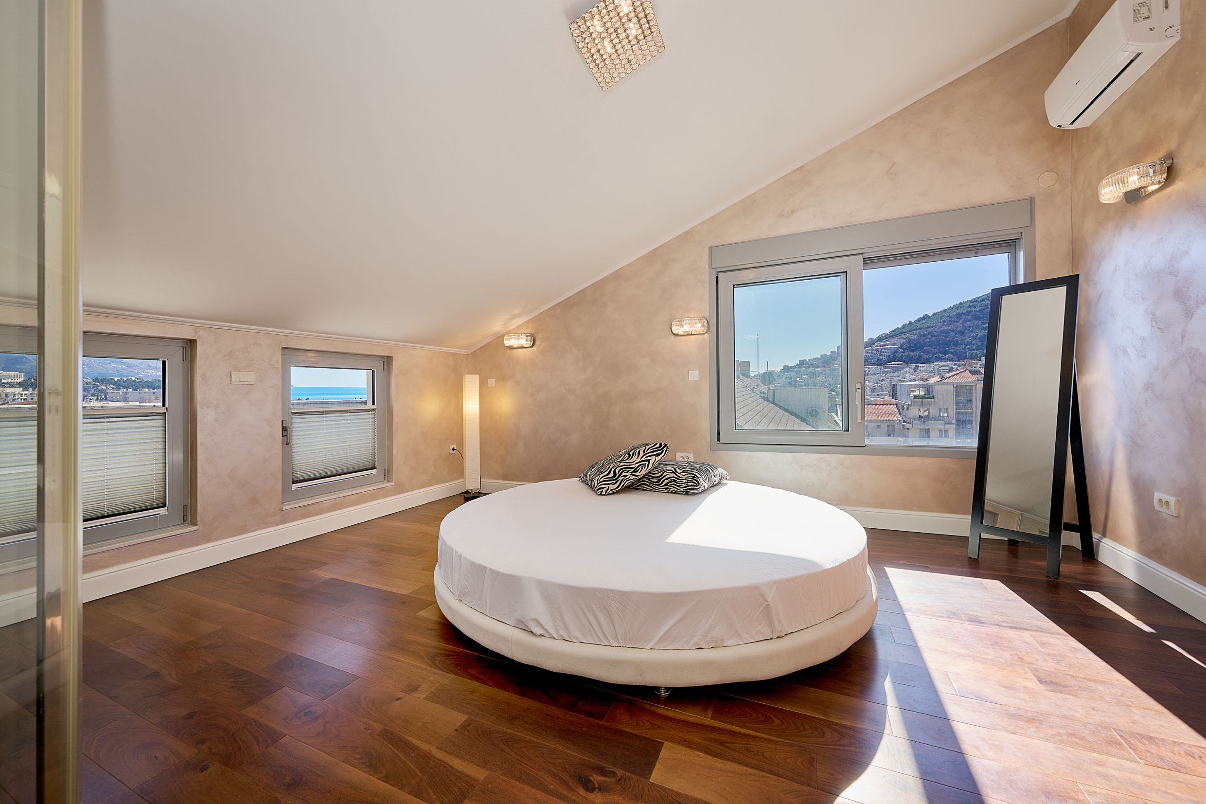 Bedroom with a round bed and sea view in an apartment in Budva, Montenegro. Attic floor, parquet flooring, modern design.