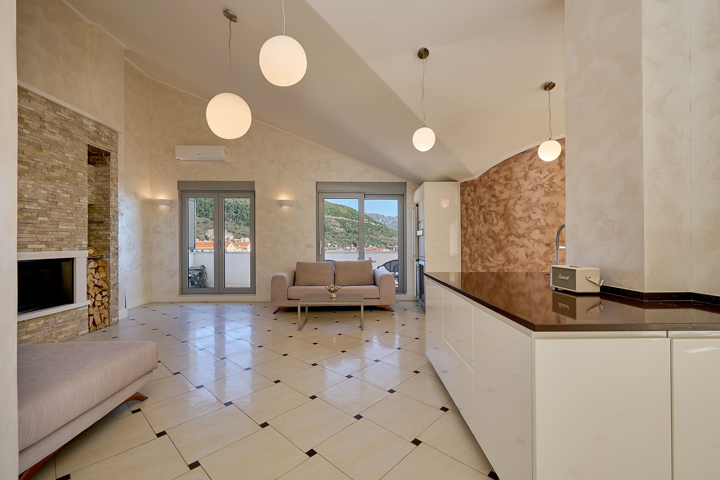 Living room with fireplace and kitchen in an apartment in Budva, Montenegro: modern interior, panoramic mountain view, and terrace.