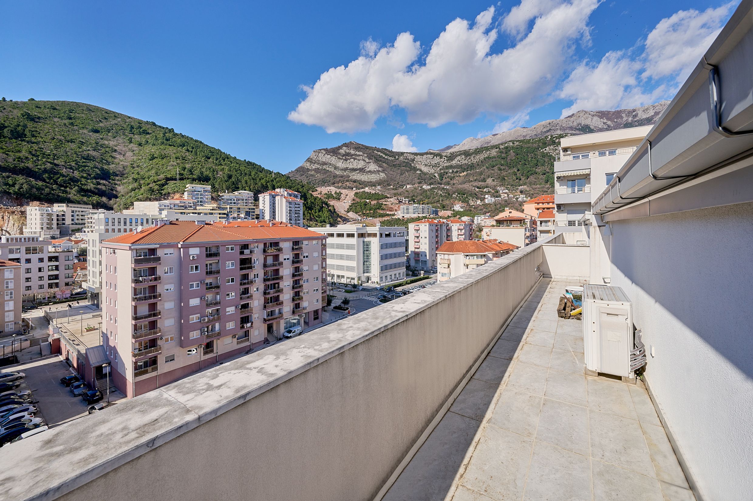 Spacious apartment balcony in Budva, Montenegro, with panoramic views of the city buildings and mountain scenery.