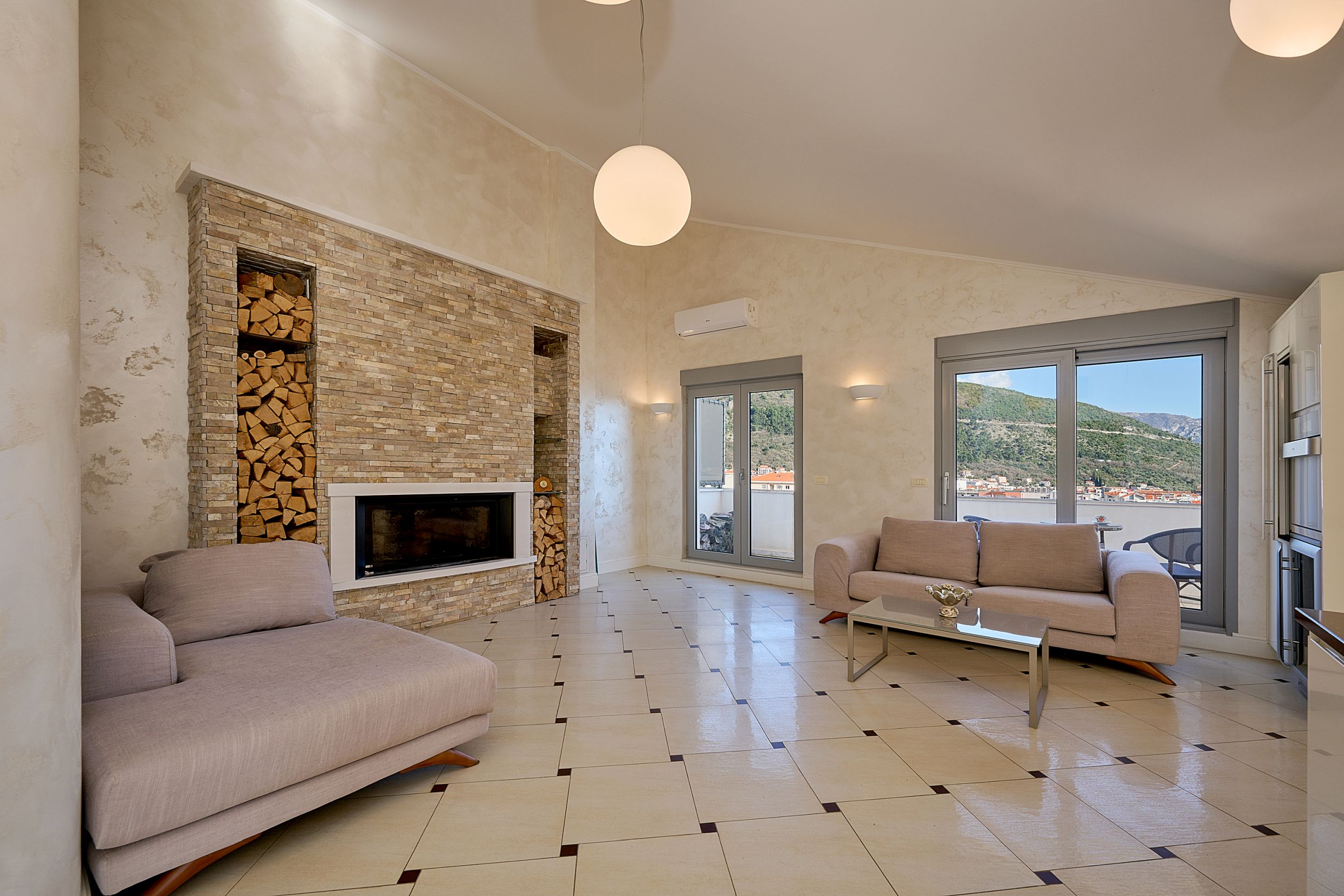 Living room with a fireplace, stone finishes, and mountain views in an apartment in Budva, Montenegro. Modern interior.