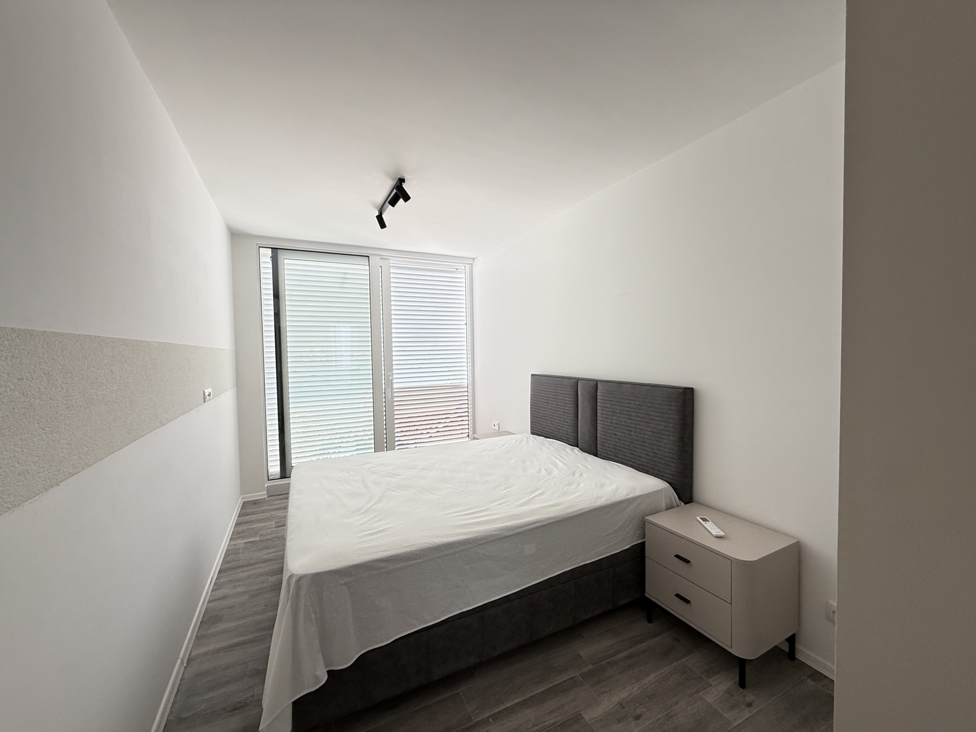 Modern bedroom with a gray double bed, nightstand, and panoramic window in a townhouse in Luštica, Montenegro.