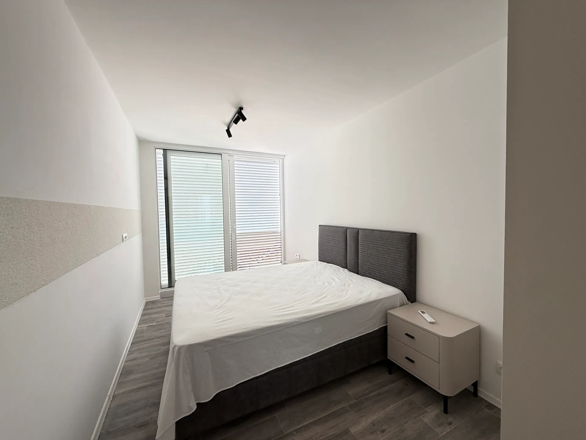 Modern bedroom featuring a double bed with a grey upholstered headboard and a light beige nightstand.