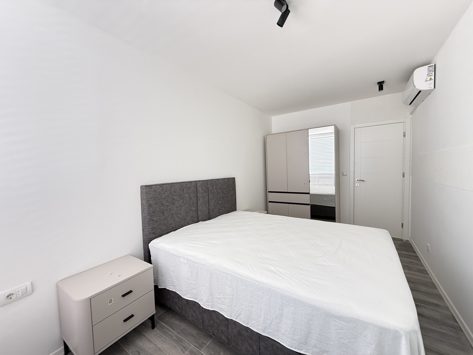 Bright bedroom in a townhouse in Luštica, Montenegro: double bed with upholstered headboard, nightstand, wardrobe, and air conditioner.